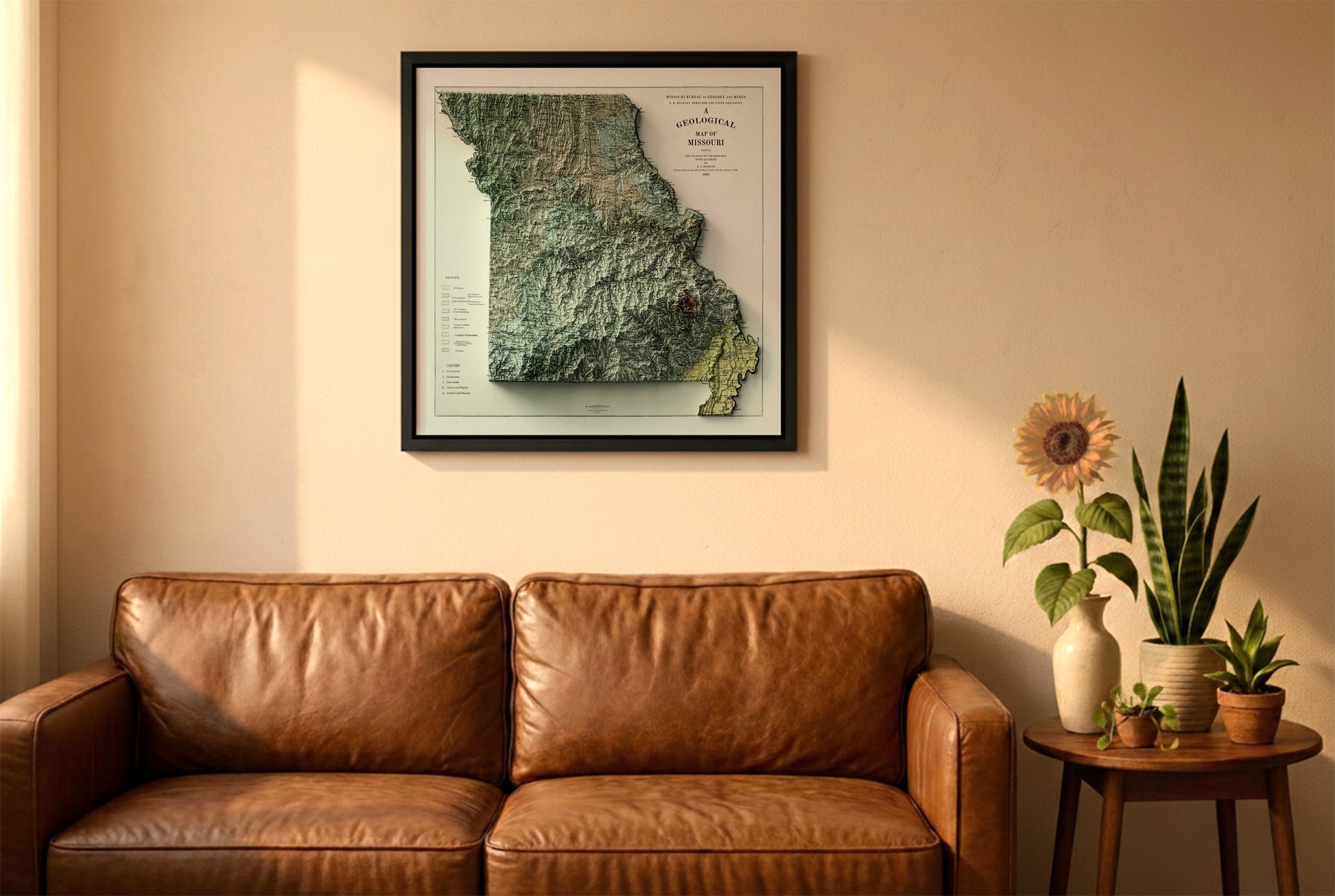 Missouri vintage relief map in a black frame above a brown leather sofa. Boho living room with warm sunlight, sunflower, and indoor plants on a wooden side table