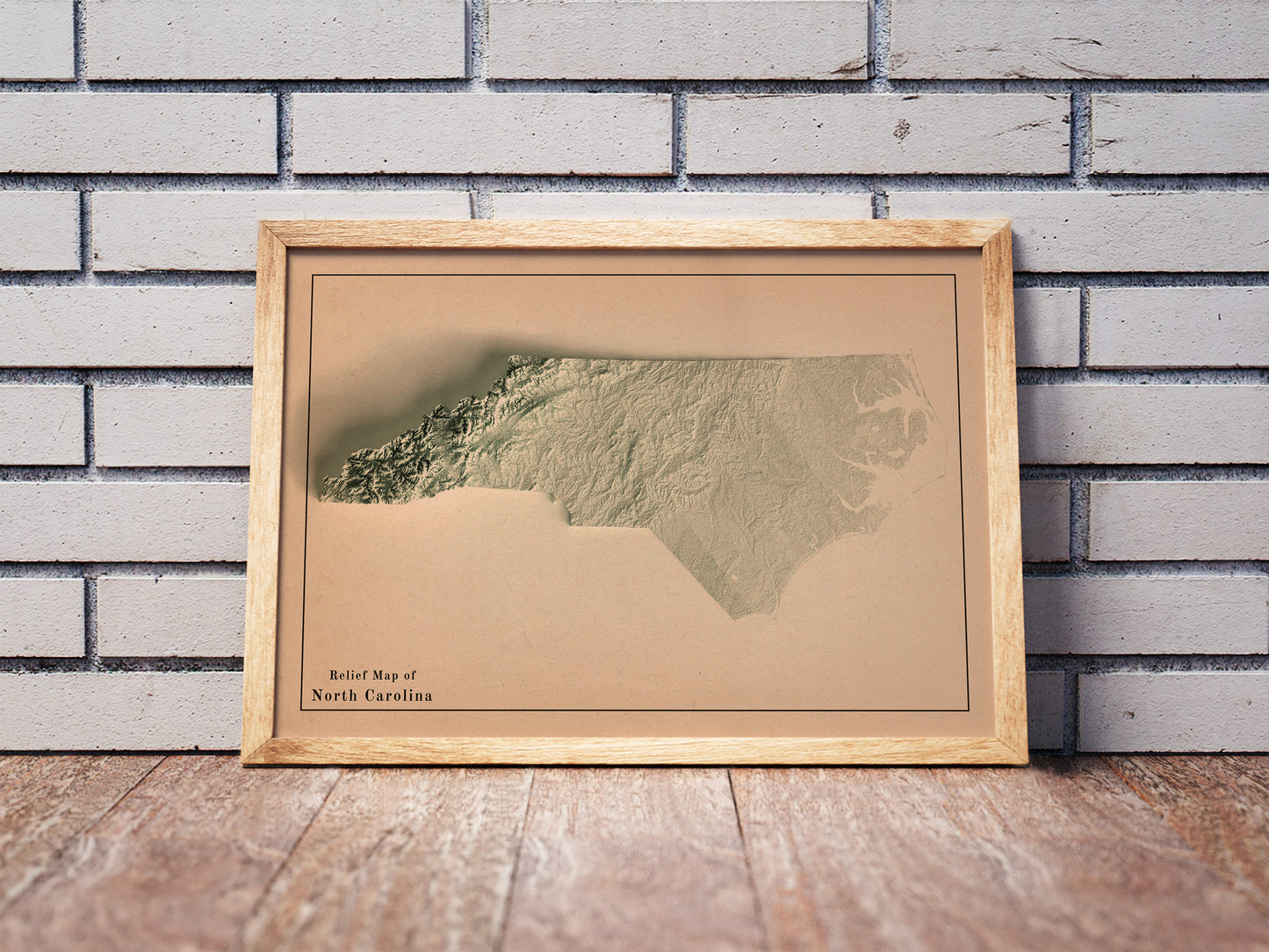 Vintage North Carolina shaded relief map in a wooden frame. Realistic terrain art print for home decor, displayed against a brick wall