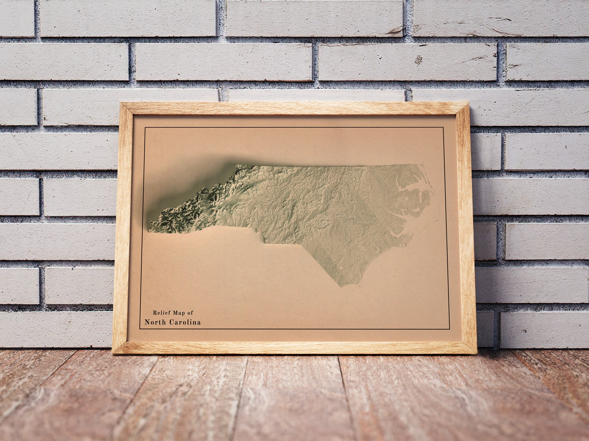 Vintage North Carolina shaded relief map in a wooden frame. Realistic terrain art print for home decor, displayed against a brick wall