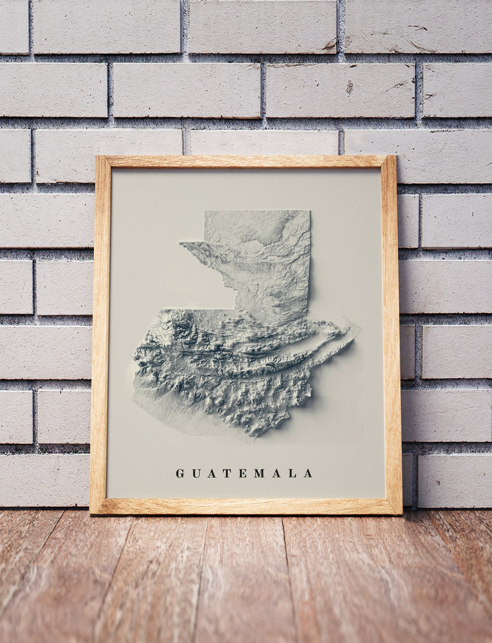 Guatemala shaded relief map in a wooden frame. Realistic terrain art print for home decor, displayed against a brick wall