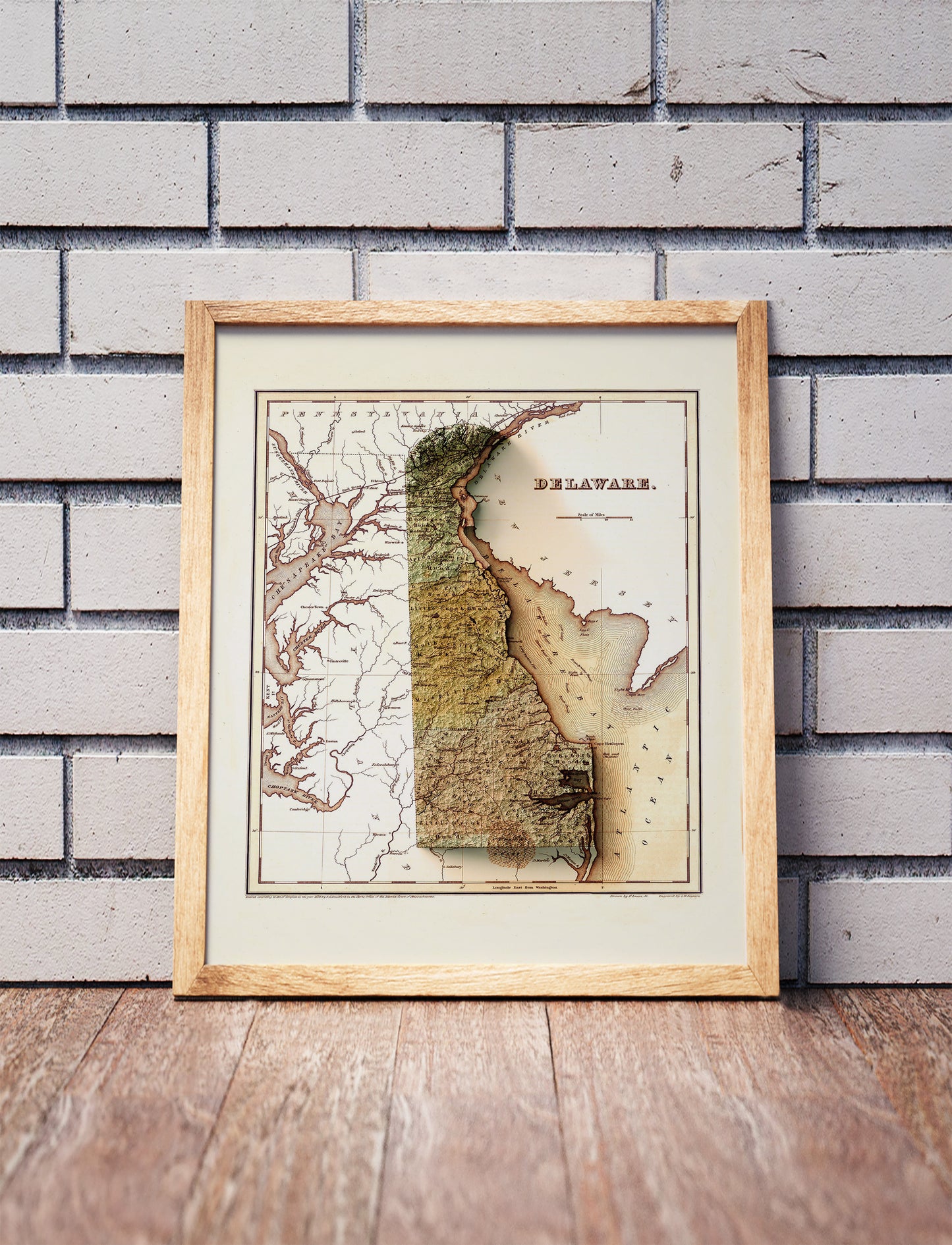 Vintage Delaware shaded relief map in a wooden frame. Realistic terrain art print for home decor, displayed against a brick wall