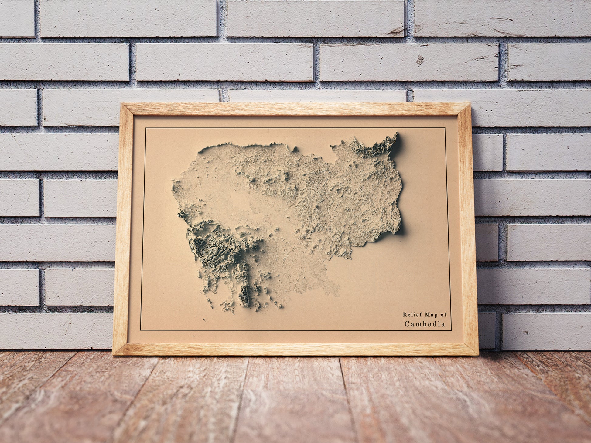 Vintage Cambodia shaded relief map in a wooden frame. Realistic terrain art print for home decor, displayed against a brick wall