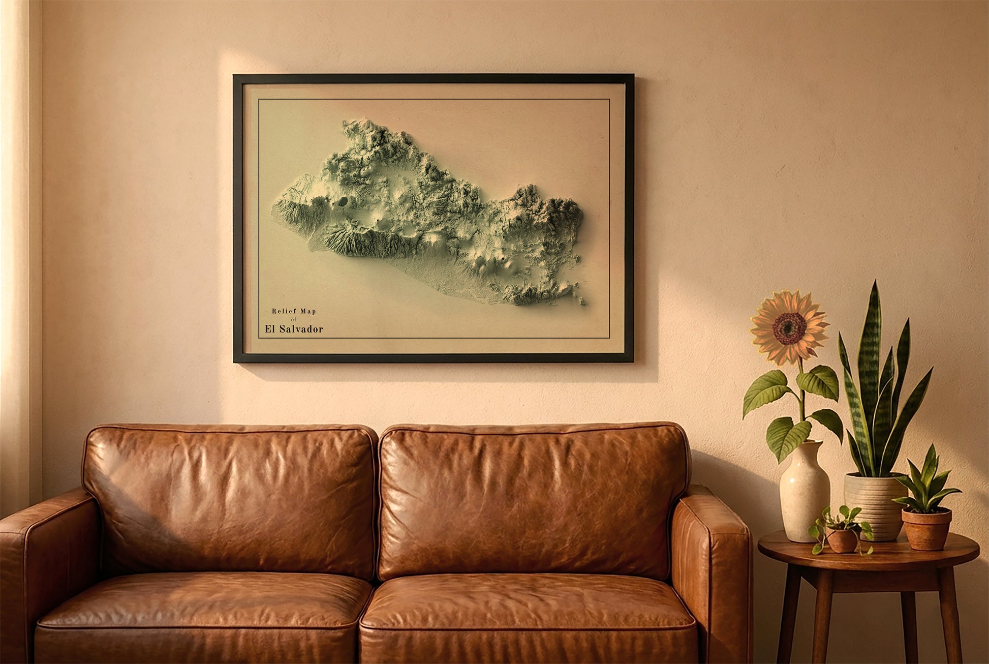 El Salvador vintage relief map in a black frame above a brown leather sofa. Boho living room with warm sunlight, sunflower, and indoor plants on a wooden side table