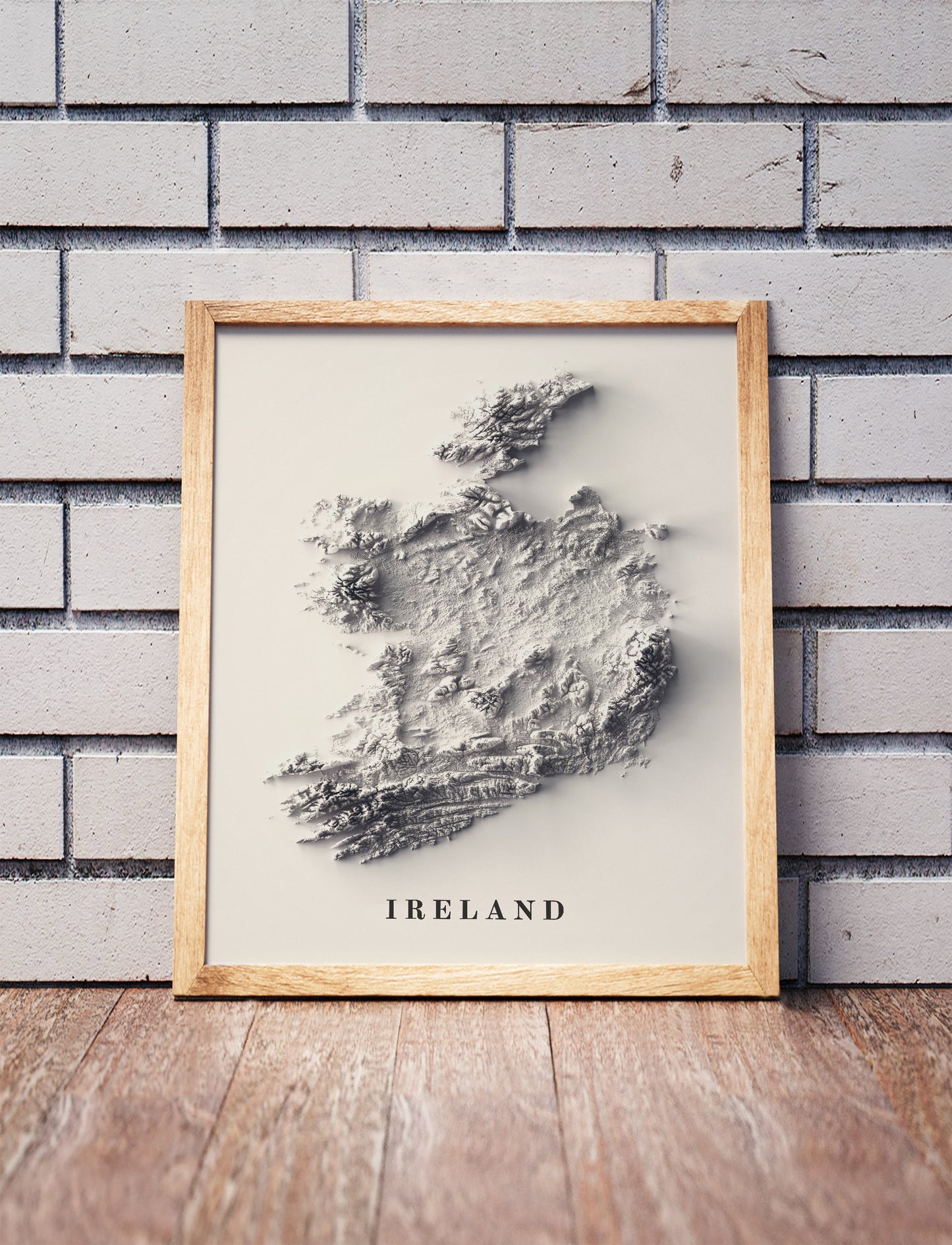 Ireland shaded relief map in a wooden frame. Realistic terrain art print for home decor, displayed against a brick wall