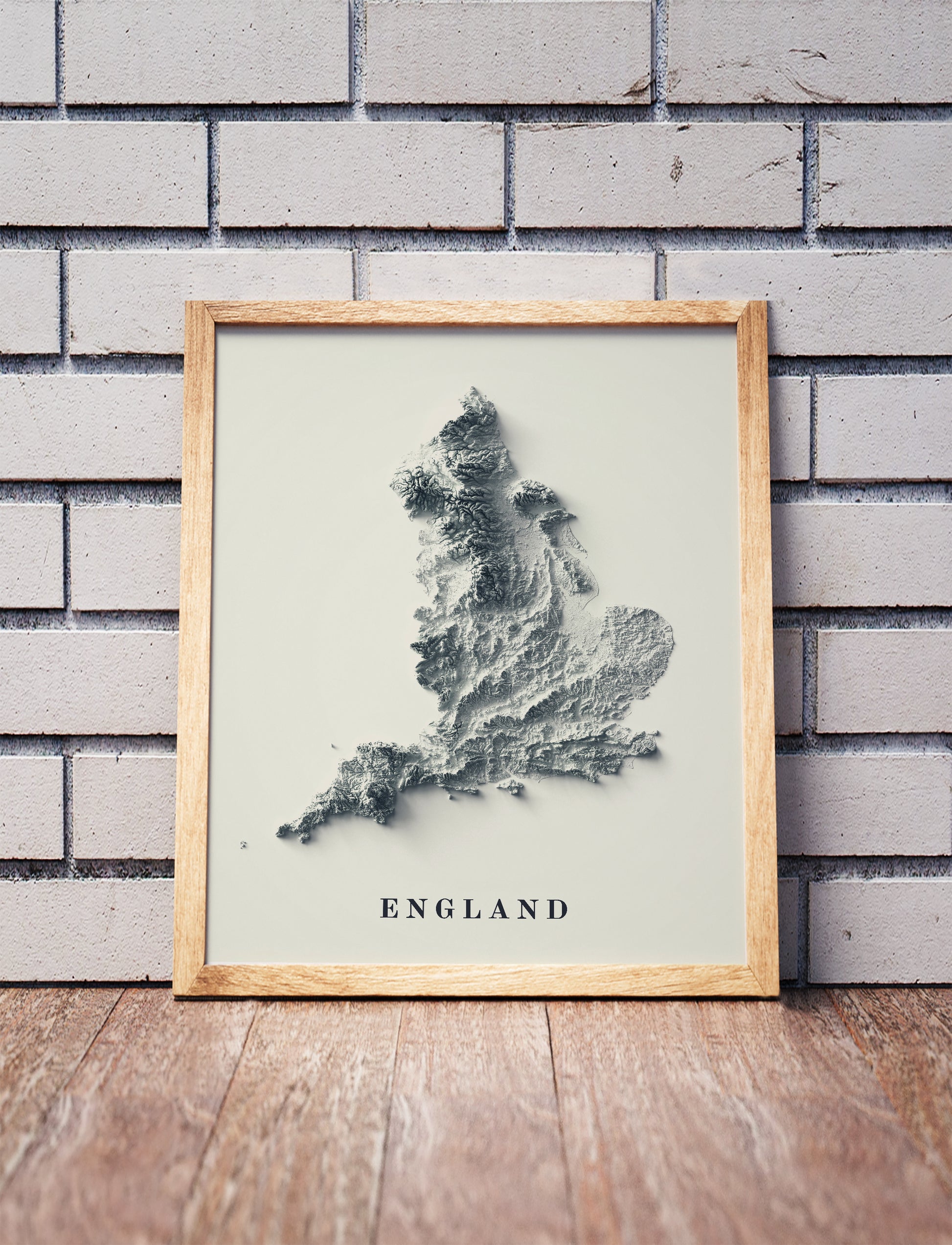 England shaded relief map in a wooden frame. Realistic terrain art print for home decor, displayed against a brick wall