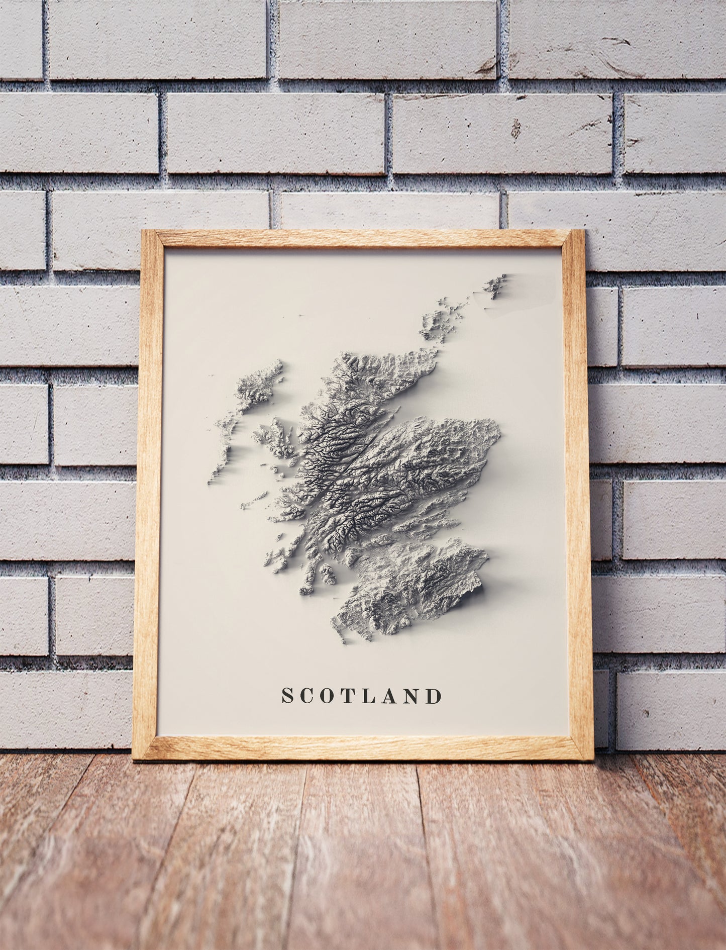 Scotland shaded relief map in a wooden frame. Realistic terrain art print for home decor, displayed against a brick wall