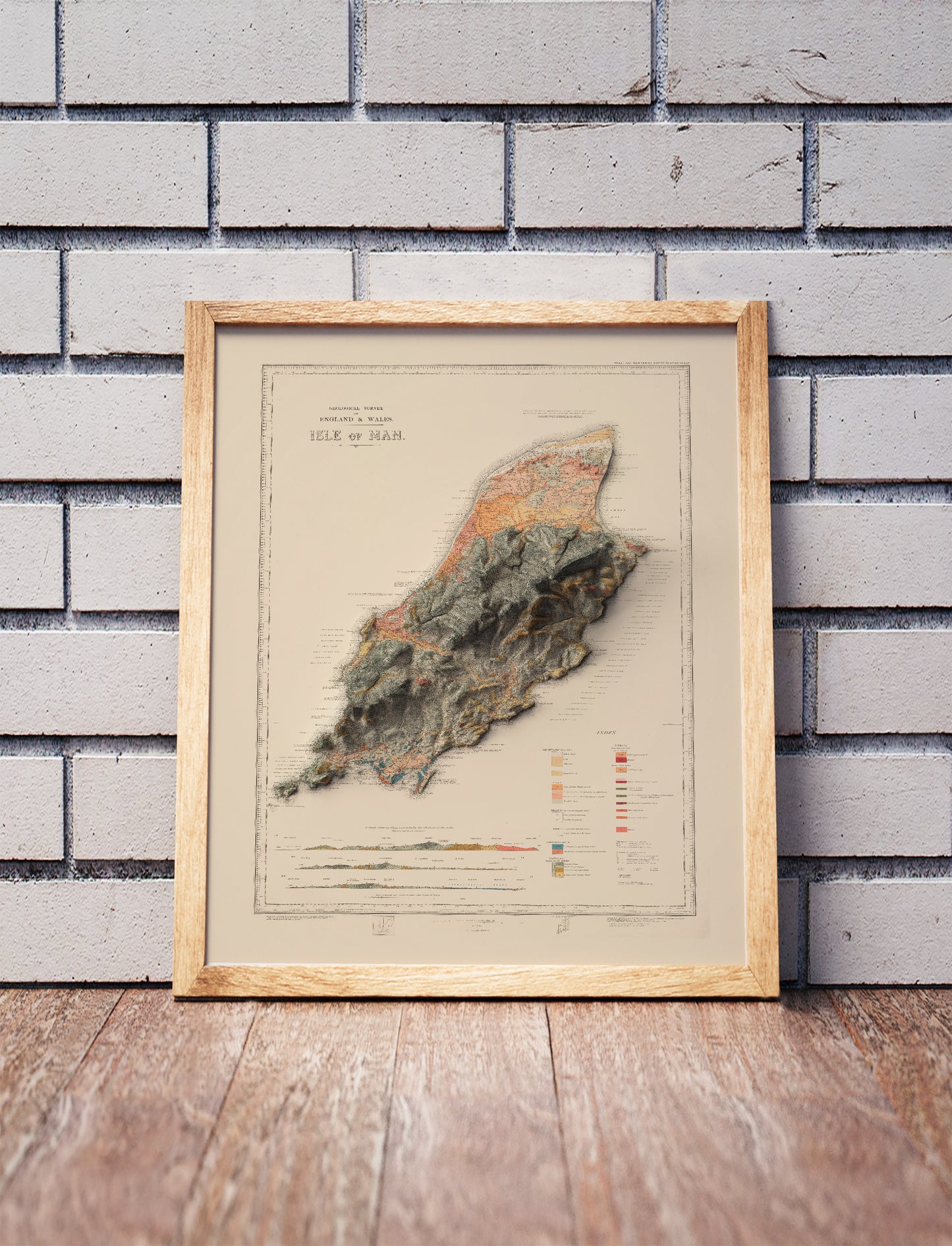 Vintage Isle of Man shaded relief map in a wooden frame. Realistic terrain art print for home decor, displayed against a brick wall