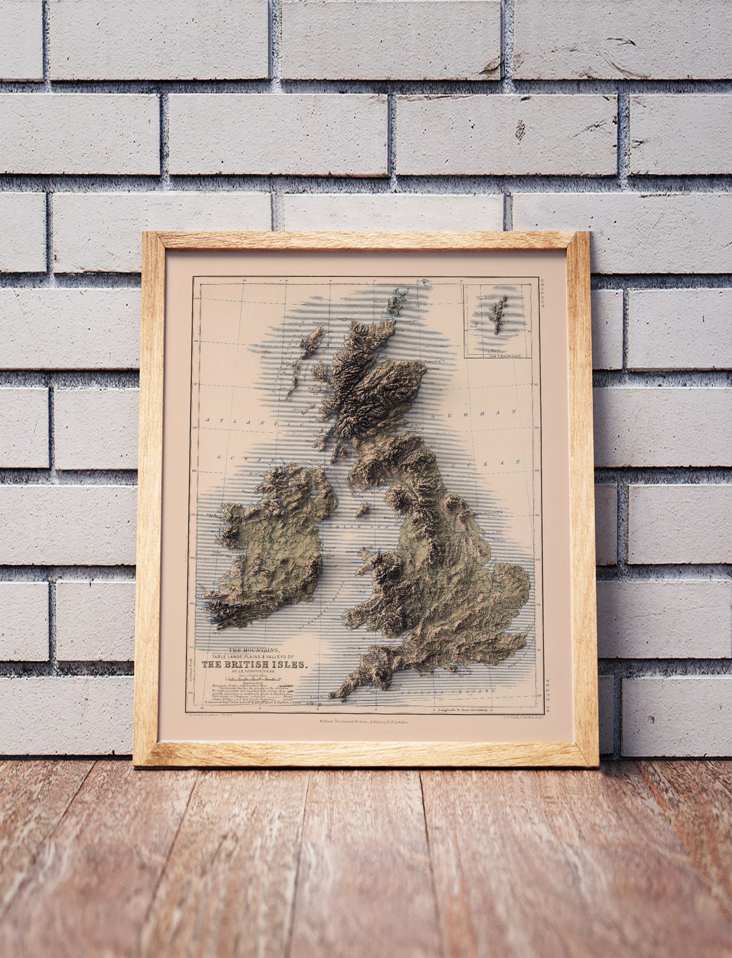 british isles vintage shaded relief map in a wooden frame. Realistic terrain art print for home decor, displayed against a brick wall