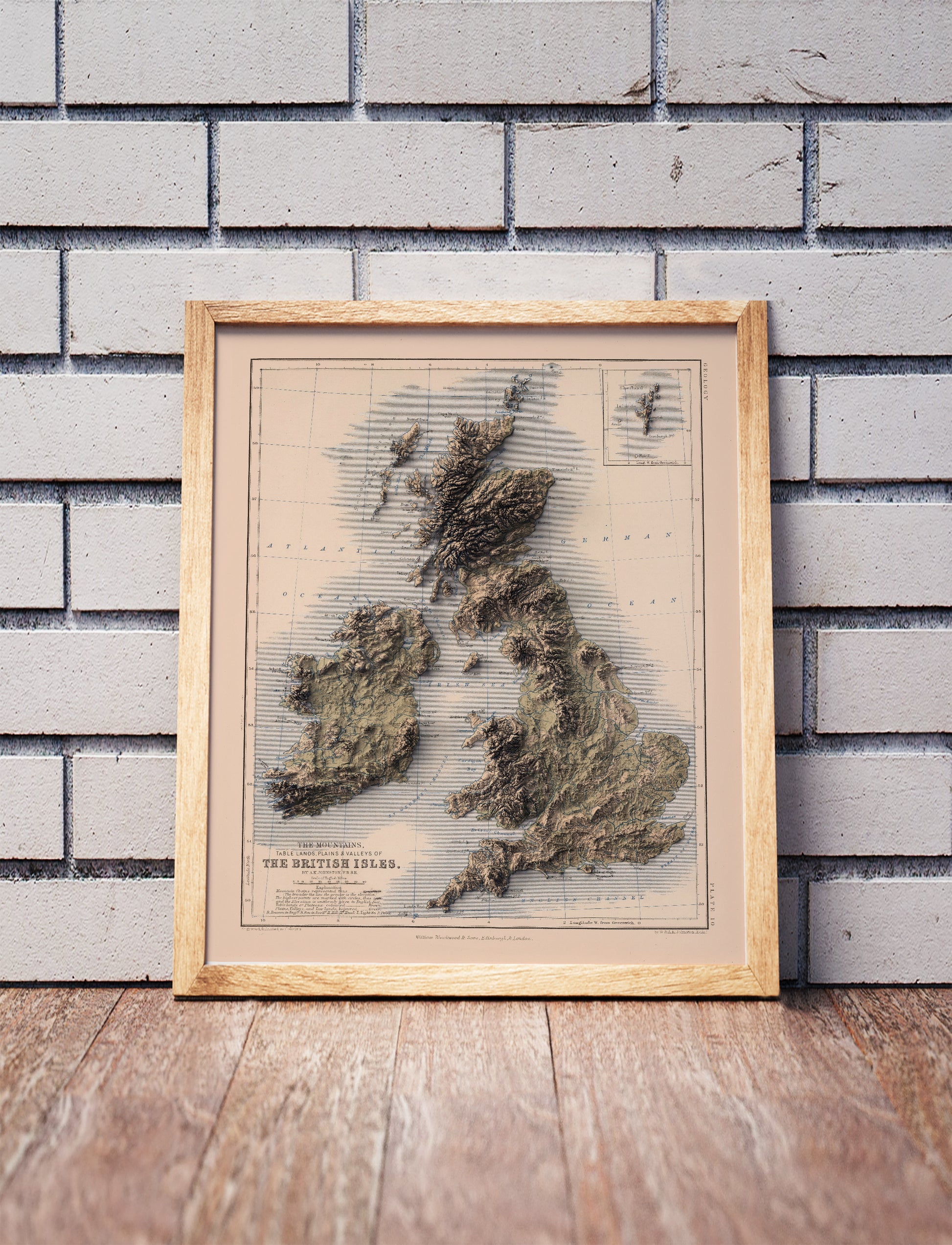british isles vintage shaded relief map in a wooden frame. Realistic terrain art print for home decor, displayed against a brick wall