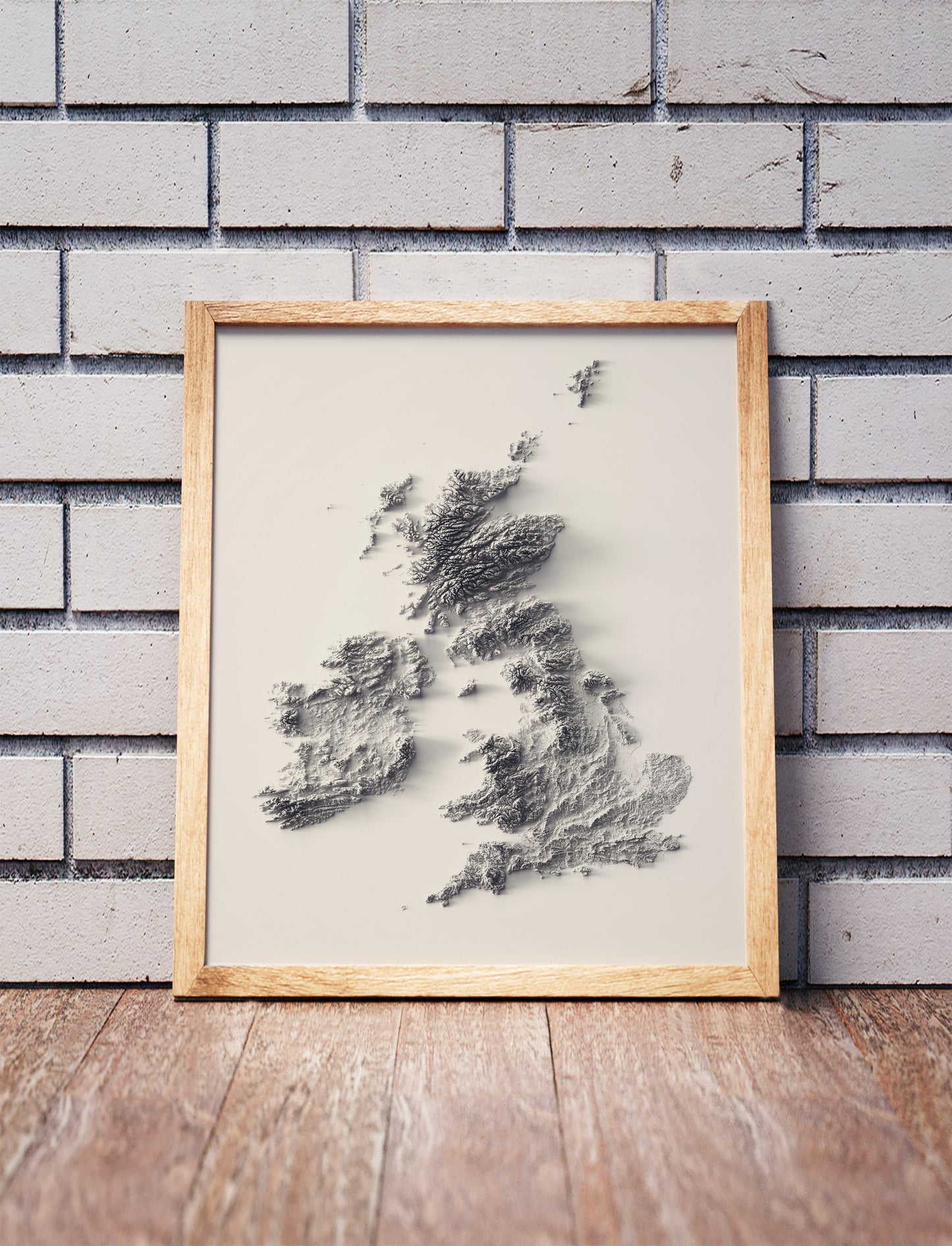 british isles shaded relief map in a wooden frame. Realistic terrain art print for home decor, displayed against a brick wall