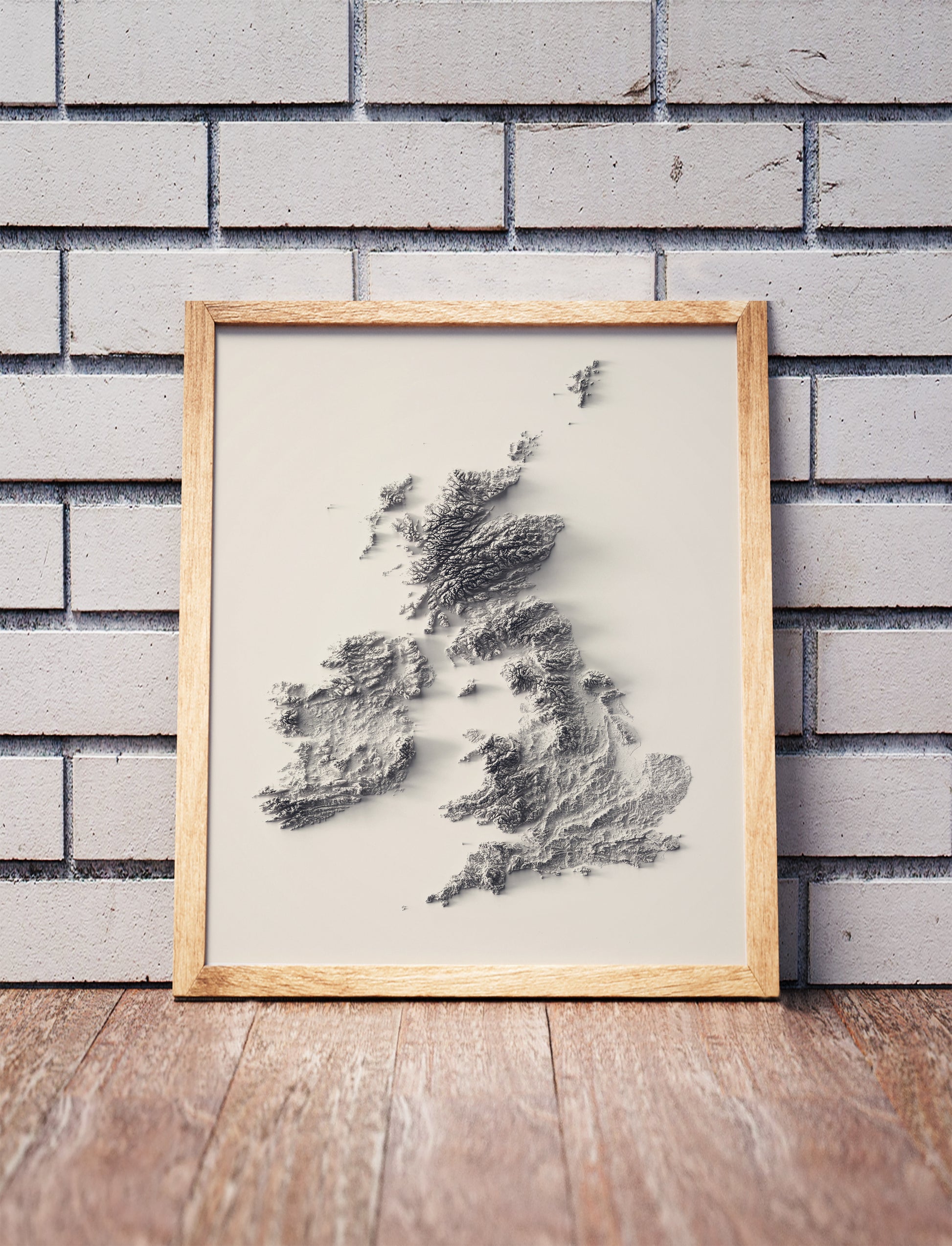 british isles shaded relief map in a wooden frame. Realistic terrain art print for home decor, displayed against a brick wall