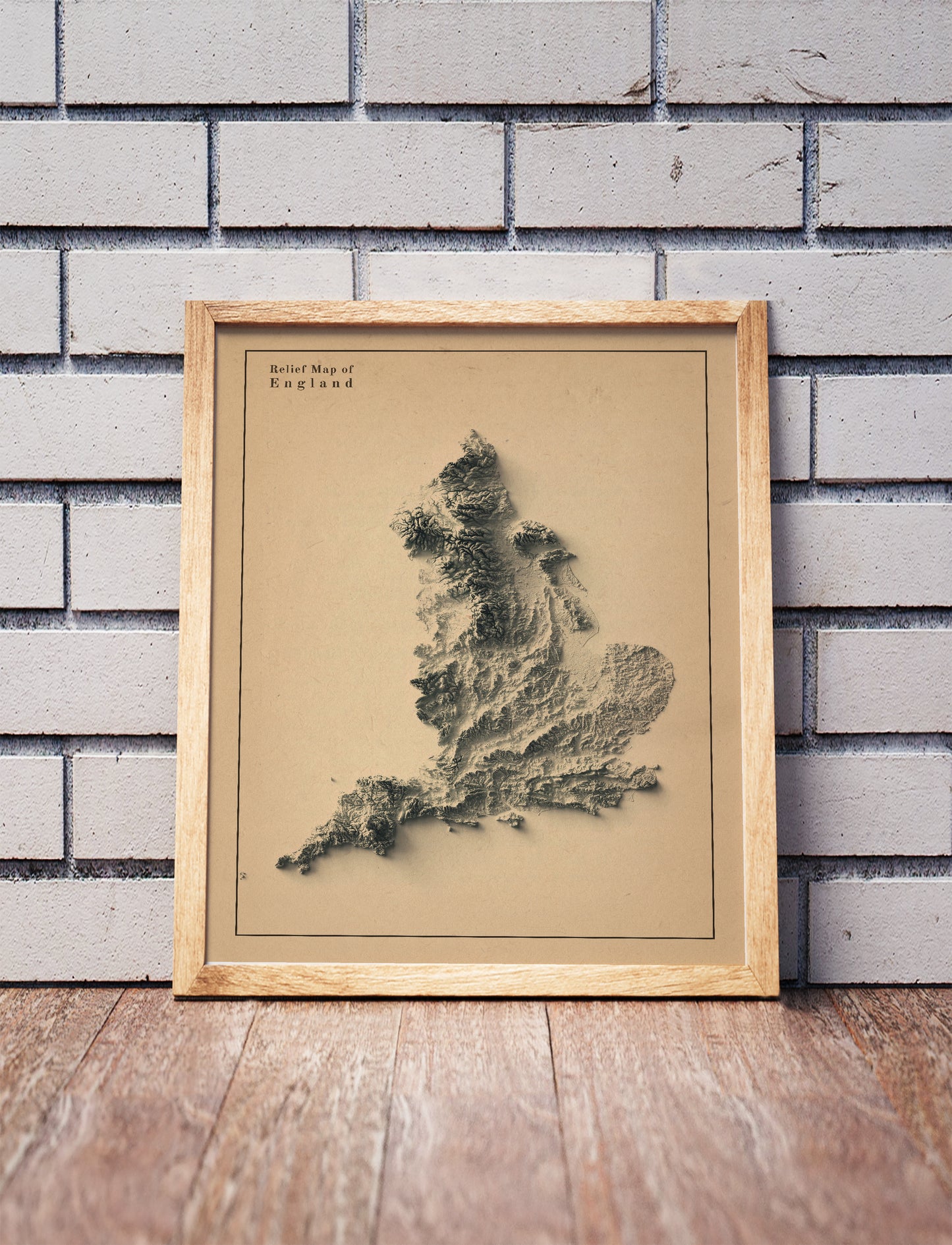 England shaded relief map in a wooden frame. Realistic terrain art print for home decor, displayed against a brick wall
