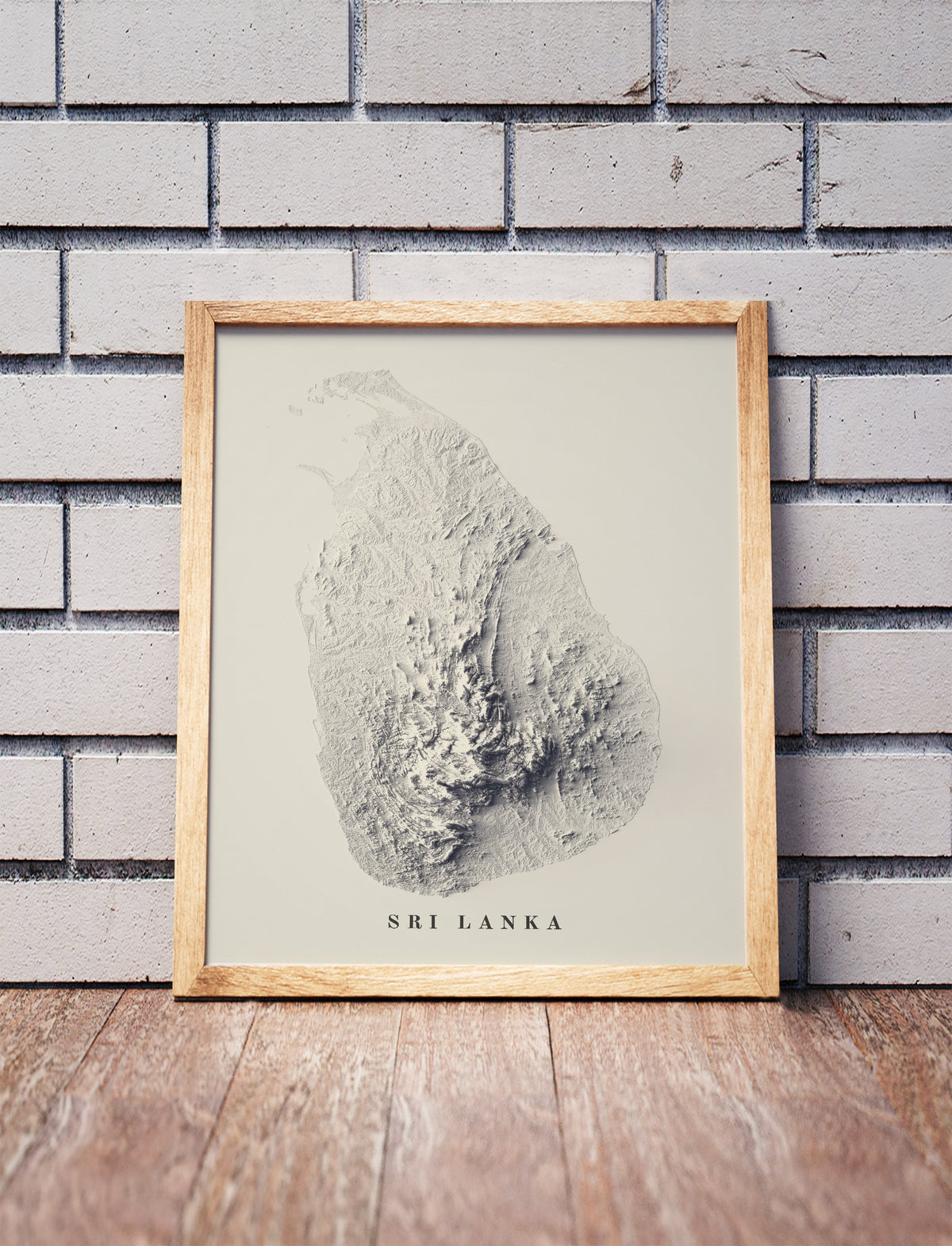 Sri Lanka shaded relief map in a wooden frame. Realistic terrain art print for home decor, displayed against a brick wall