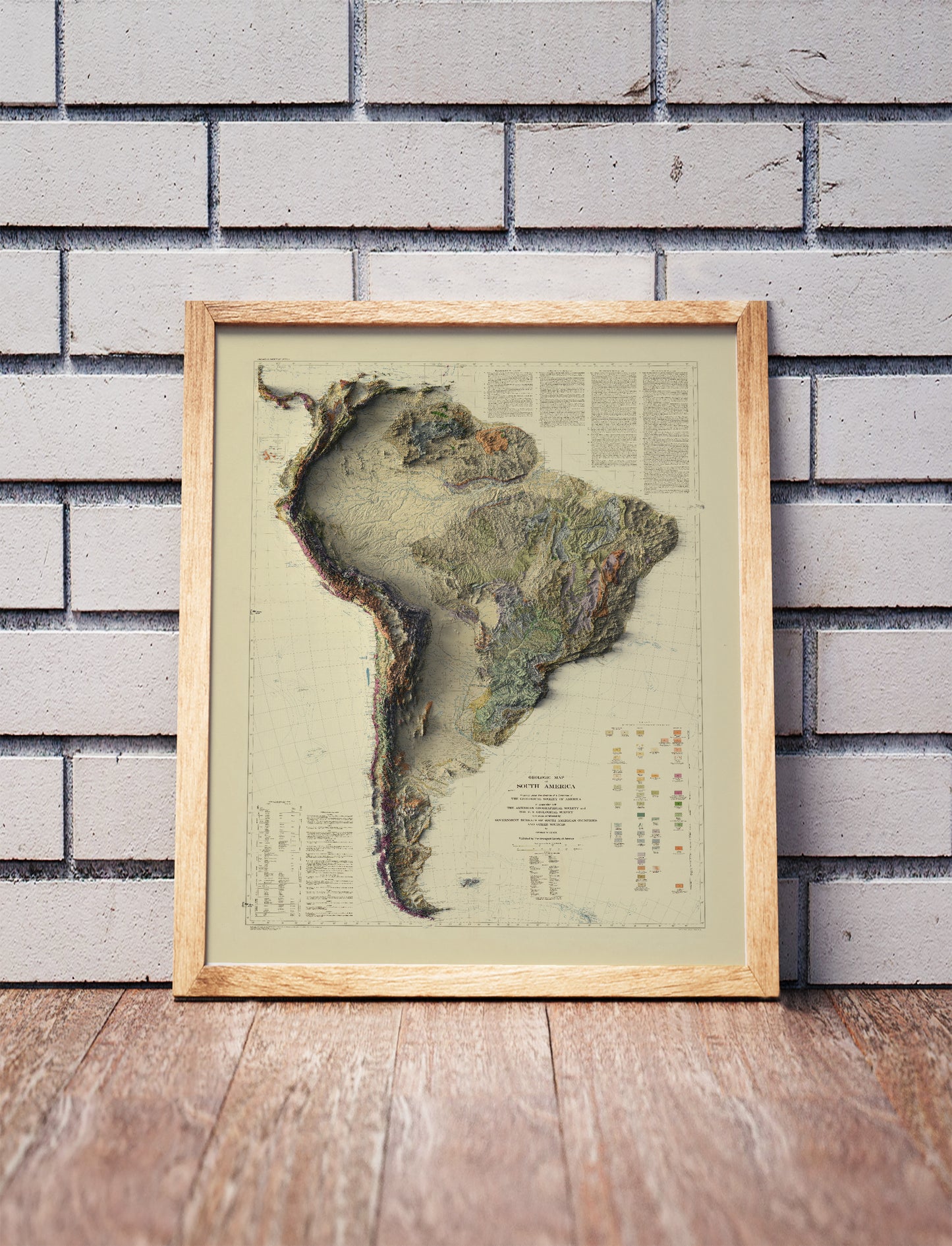 Vintage South America shaded relief map in a wooden frame. Realistic terrain art print for home decor, displayed against a brick wall