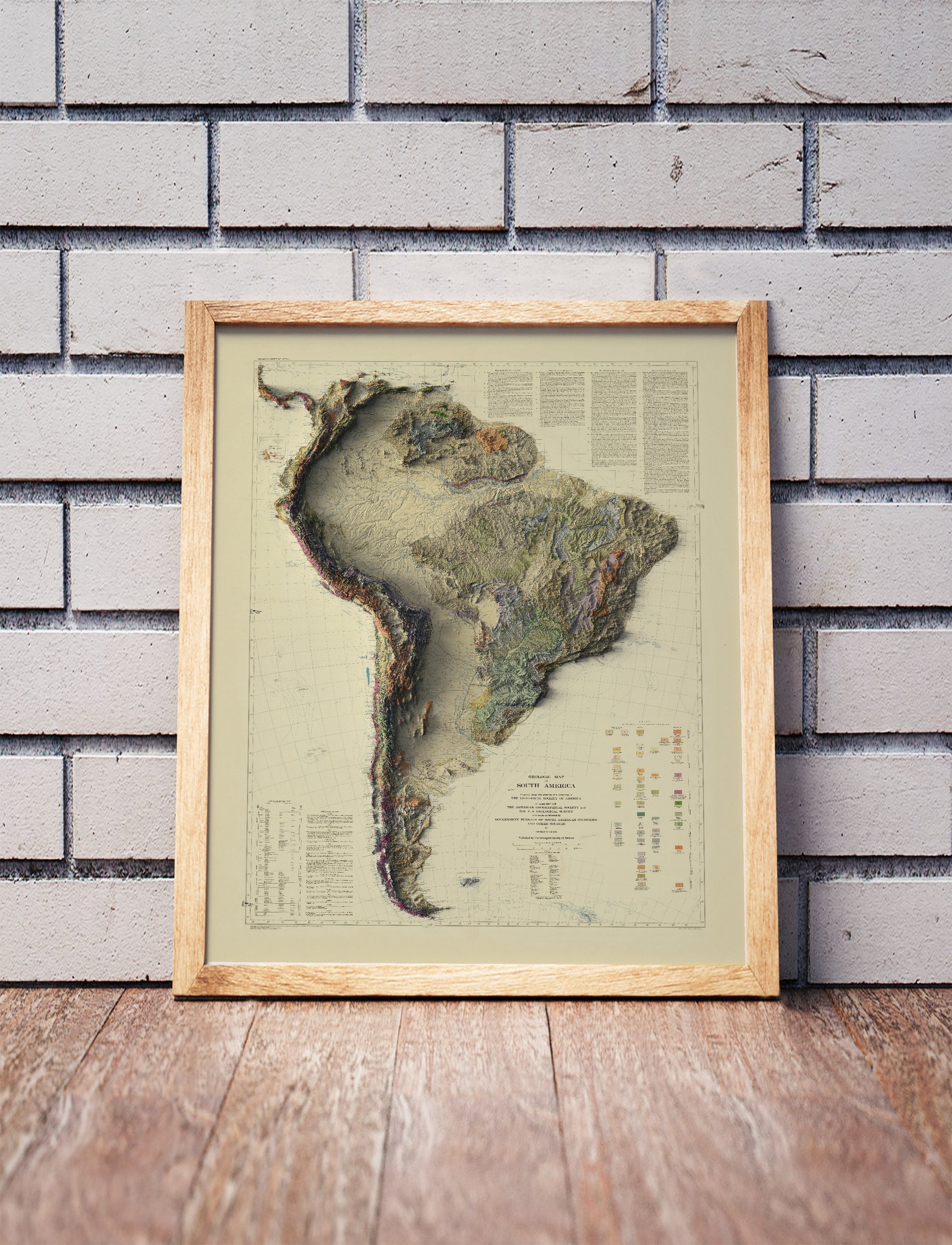 Vintage South America shaded relief map in a wooden frame. Realistic terrain art print for home decor, displayed against a brick wall