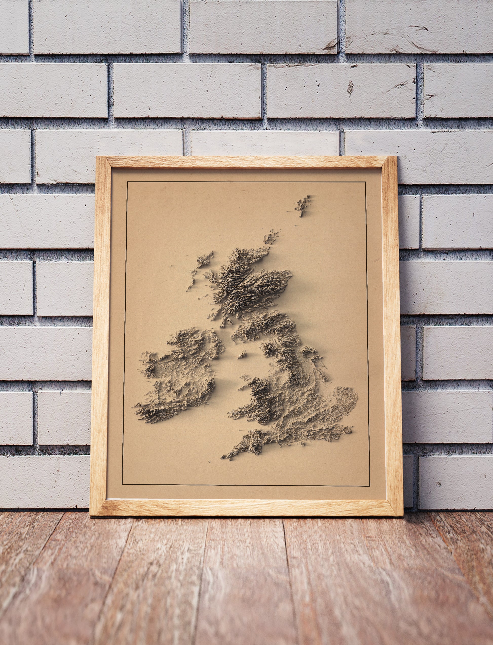 british isles shaded relief map in a wooden frame. Realistic terrain art print for home decor, displayed against a brick wall
