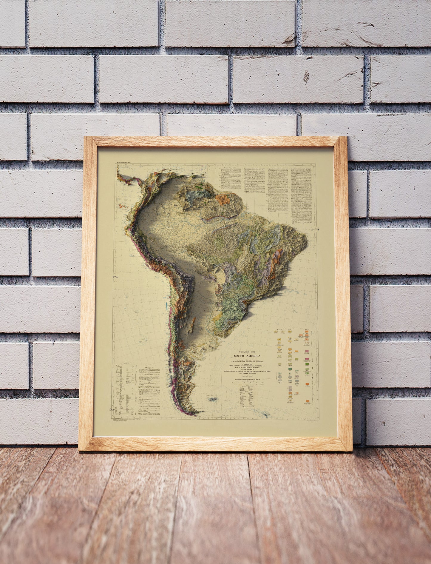 Vintage South America shaded relief map in a wooden frame. Realistic terrain art print for home decor, displayed against a brick wall