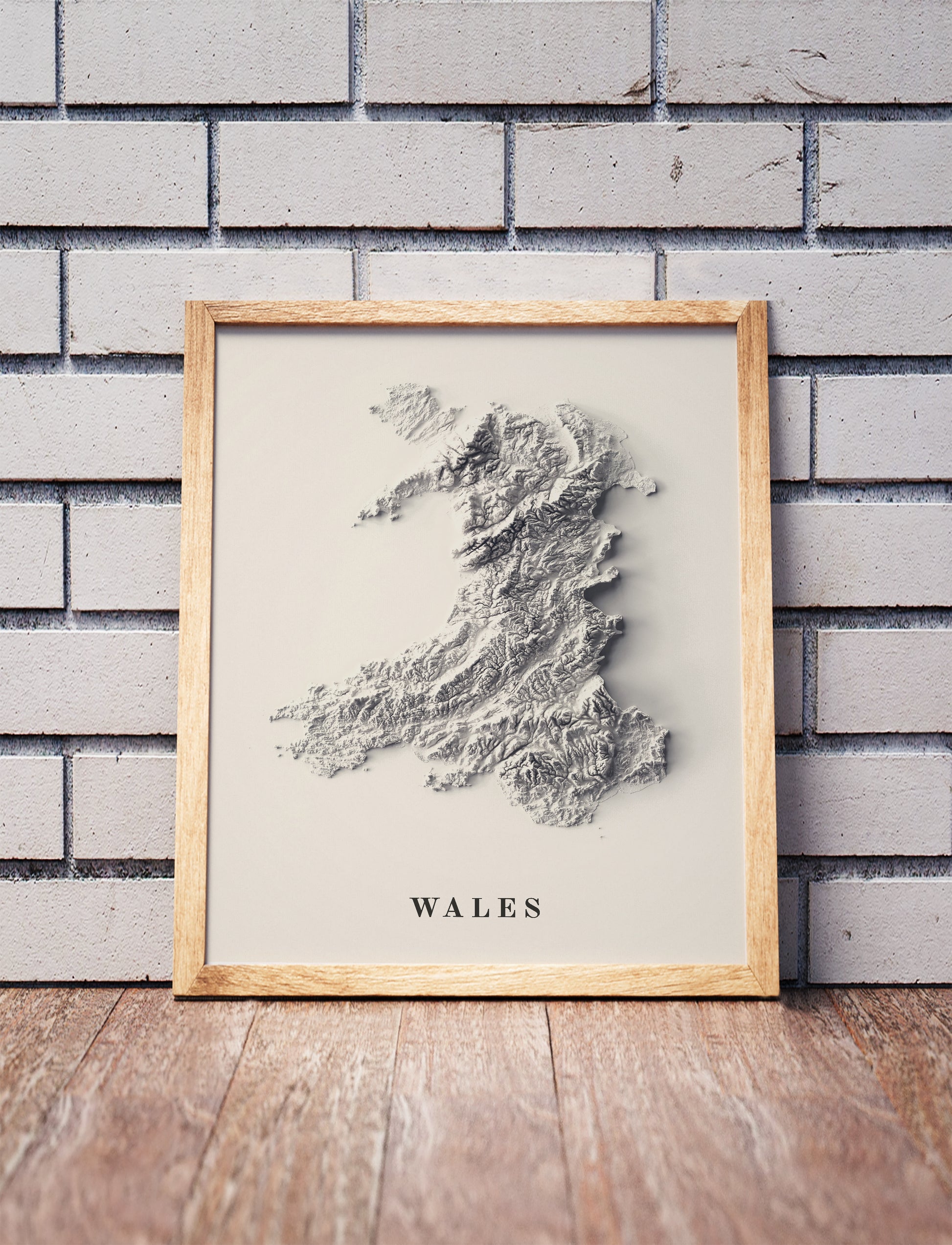 wales shaded relief map in a wooden frame. Realistic terrain art print for home decor, displayed against a brick wall