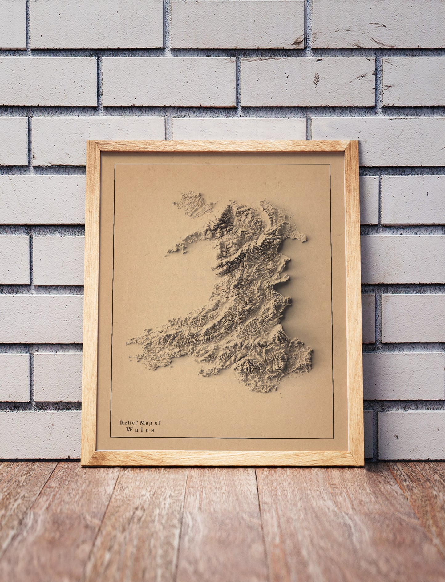 wales shaded relief map in a wooden frame. Realistic terrain art print for home decor, displayed against a brick wall