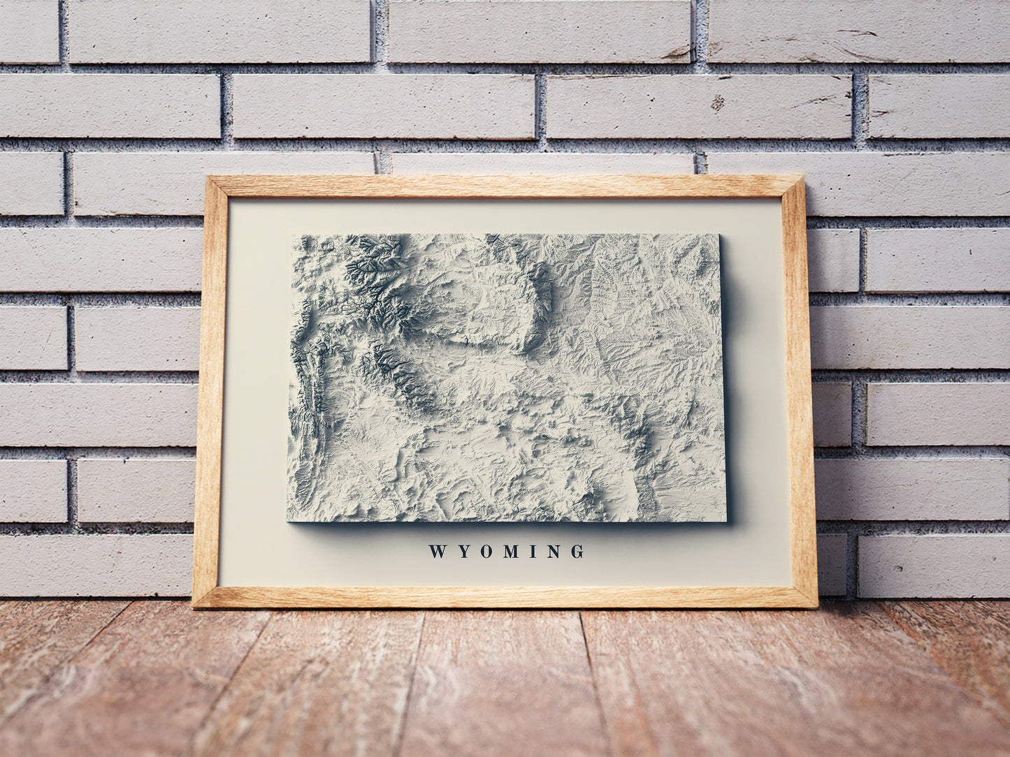 Wyoming shaded relief map in a wooden frame. Realistic terrain art print for home decor, displayed against a brick wall