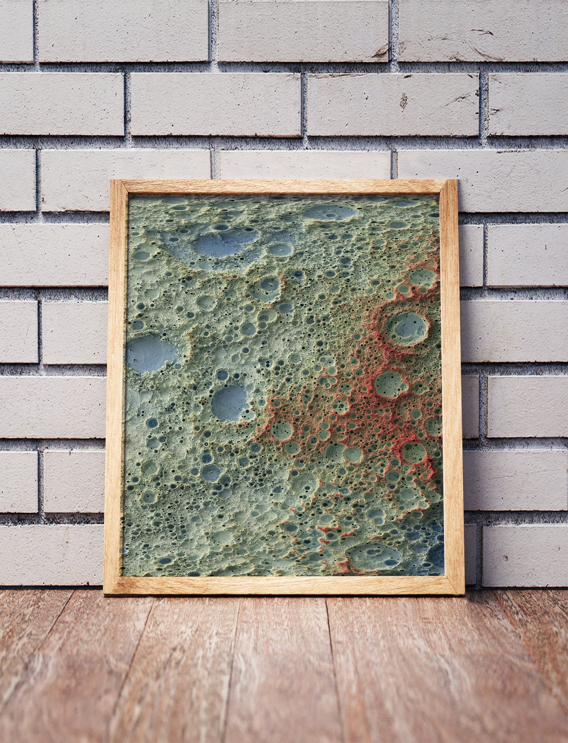 Moon shaded relief map in a wooden frame. Realistic terrain art print for home decor, displayed against a brick wall