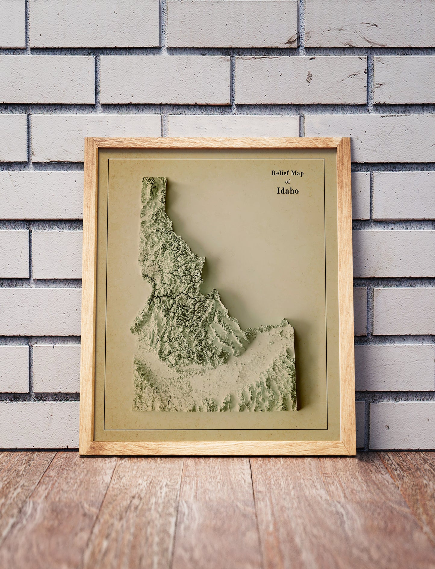 Vintage Idaho shaded relief map in a wooden frame. Realistic terrain art print for home decor, displayed against a brick wall