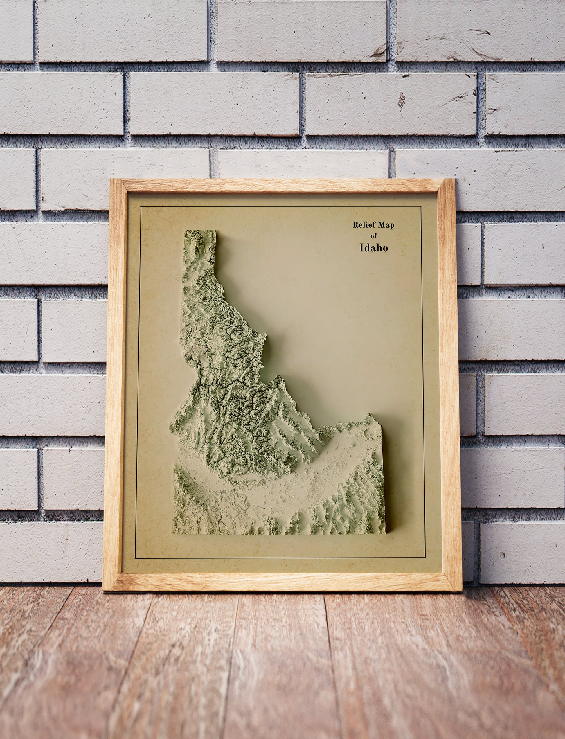 Vintage Idaho shaded relief map in a wooden frame. Realistic terrain art print for home decor, displayed against a brick wall