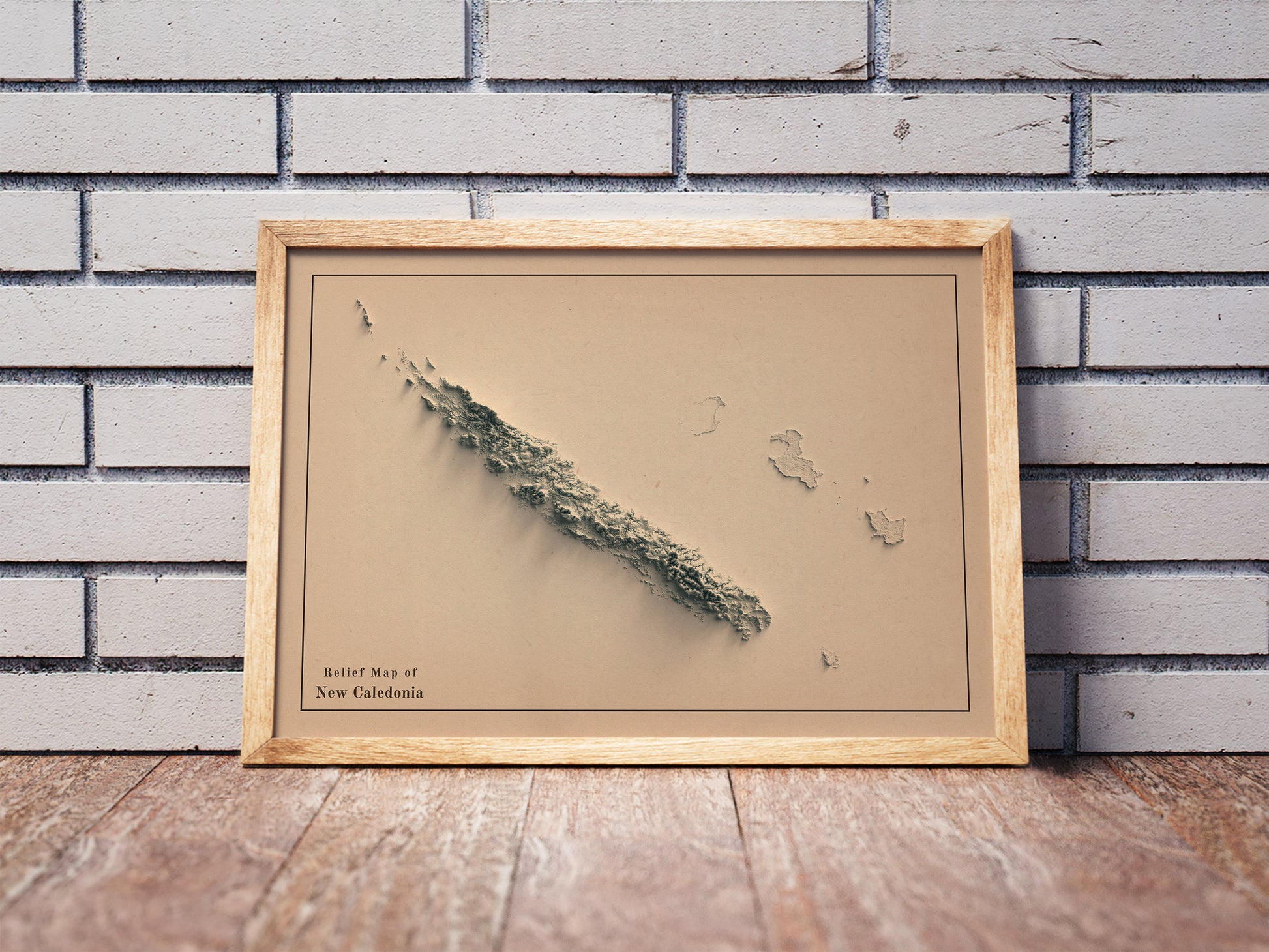 Vintage New Caledonia shaded relief map in a wooden frame. Realistic terrain art print for home decor, displayed against a brick wall