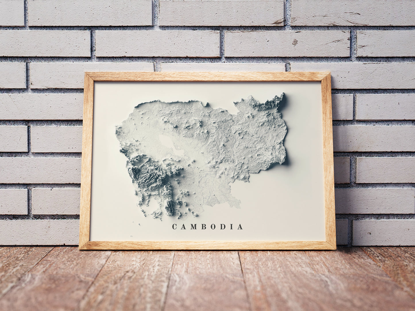 Cambodia shaded relief map in a wooden frame. Realistic terrain art print for home decor, displayed against a brick wall