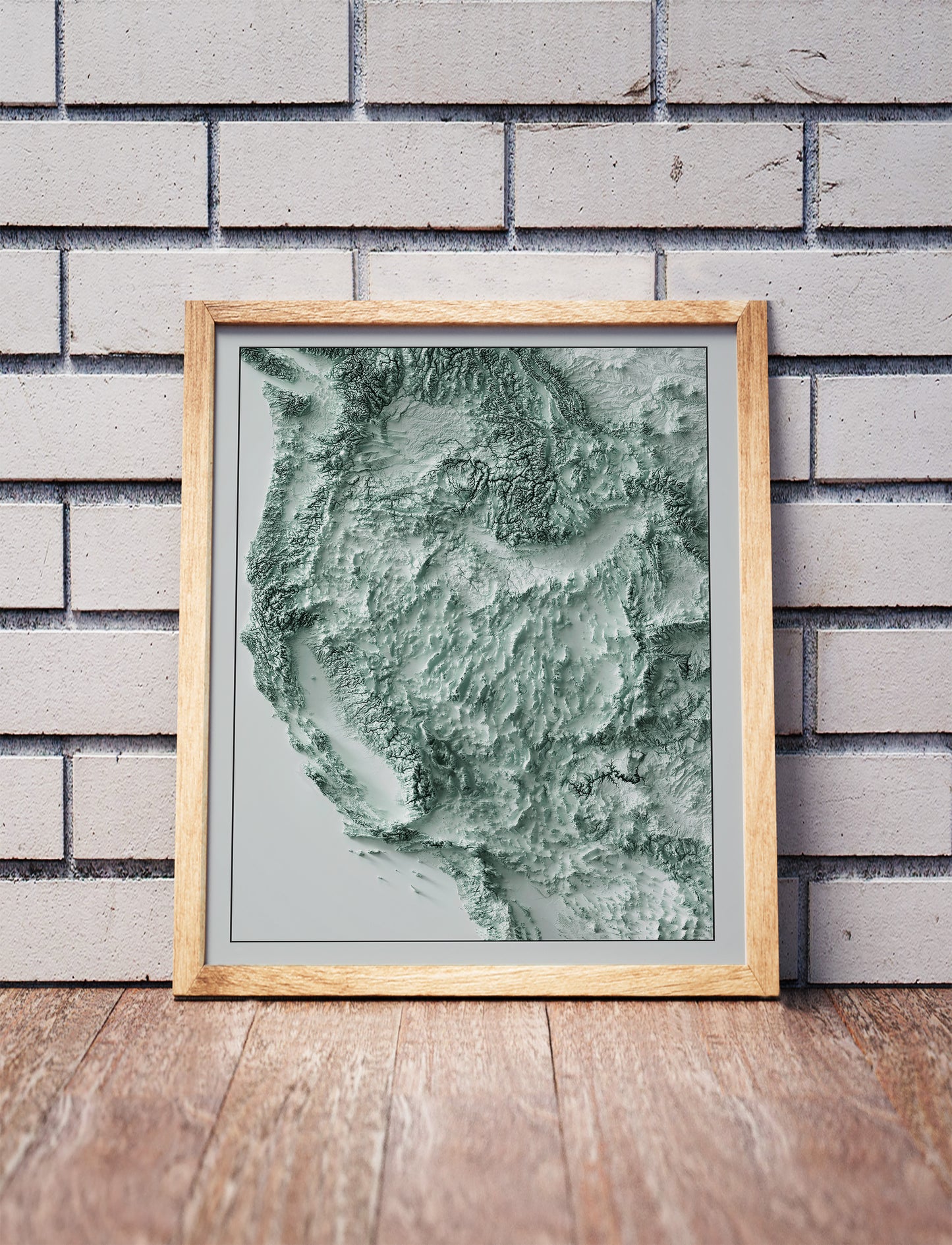 Western USA shaded relief map in a wooden frame. Realistic terrain art print for home decor, displayed against a brick wall