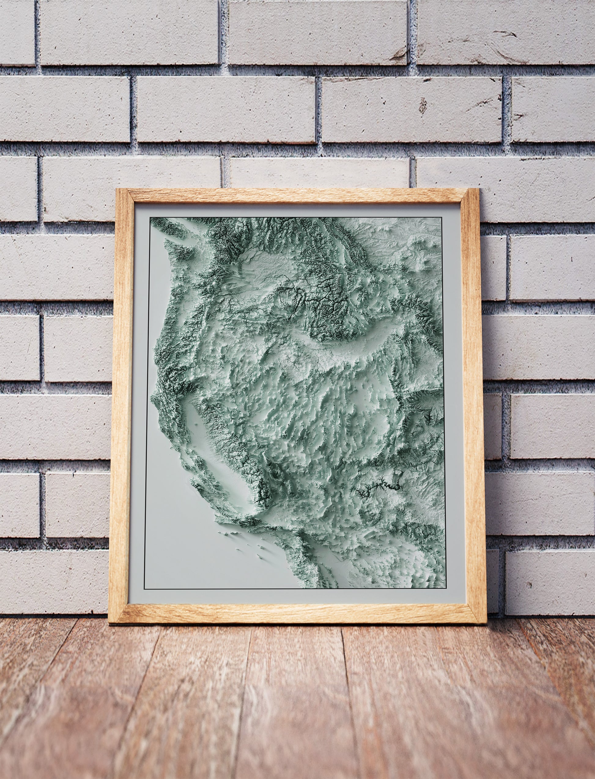 Western USA shaded relief map in a wooden frame. Realistic terrain art print for home decor, displayed against a brick wall
