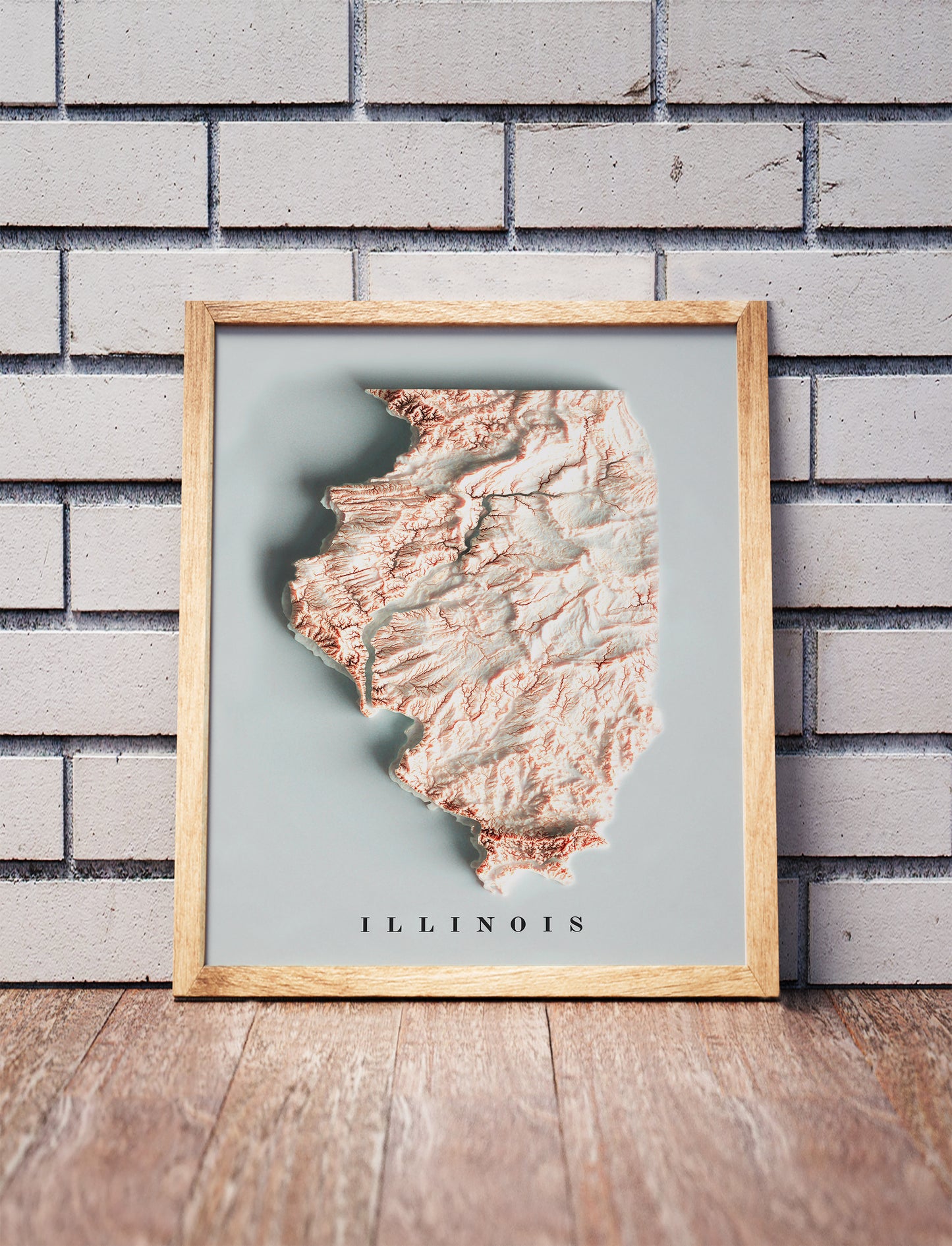 Illinois shaded relief map in a wooden frame. Realistic terrain art print for home decor, displayed against a brick wall
