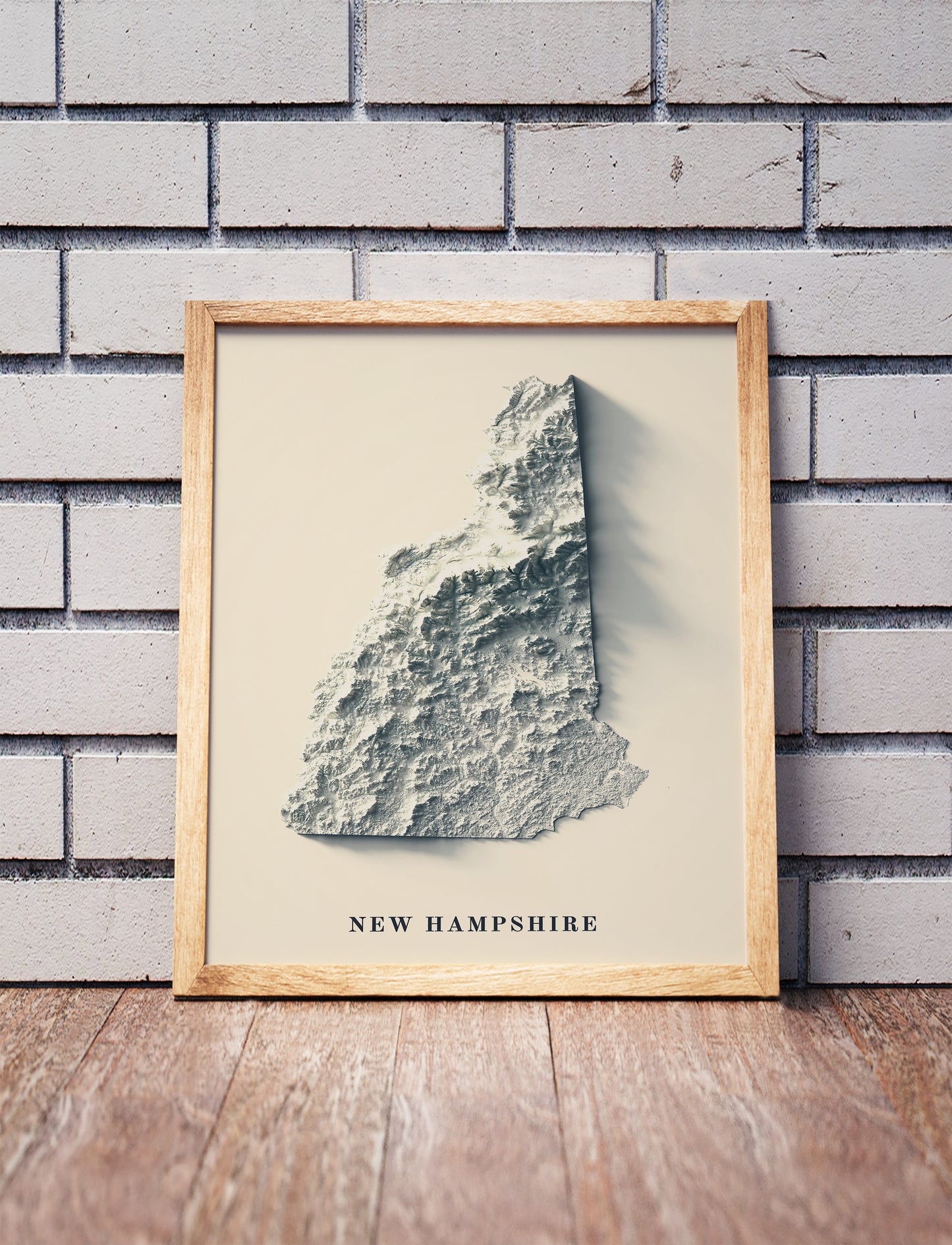 New Hampshire shaded relief map in a wooden frame. Realistic terrain art print for home decor, displayed against a brick wall
