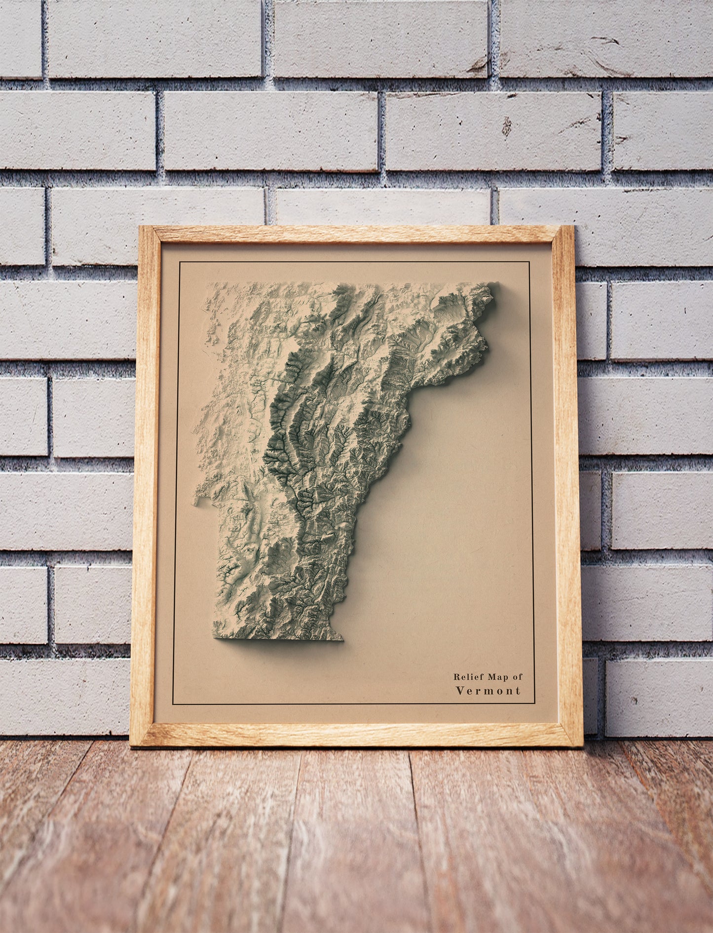Vintage Vermont shaded relief map in a wooden frame. Realistic terrain art print for home decor, displayed against a brick wall
