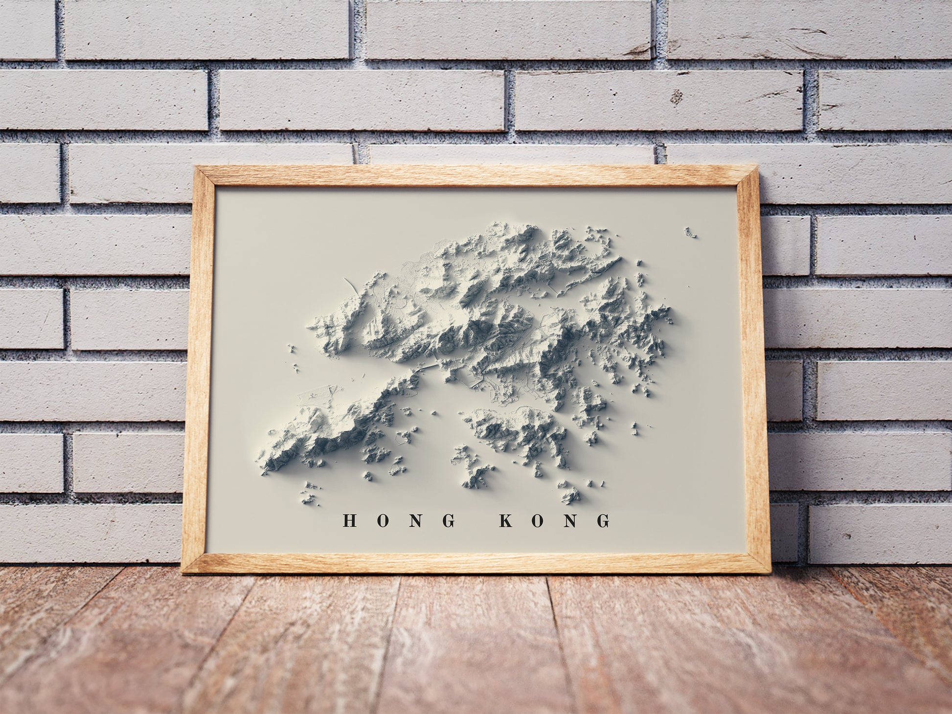 Hong Kong shaded relief map in a wooden frame. Realistic terrain art print for home decor, displayed against a brick wall