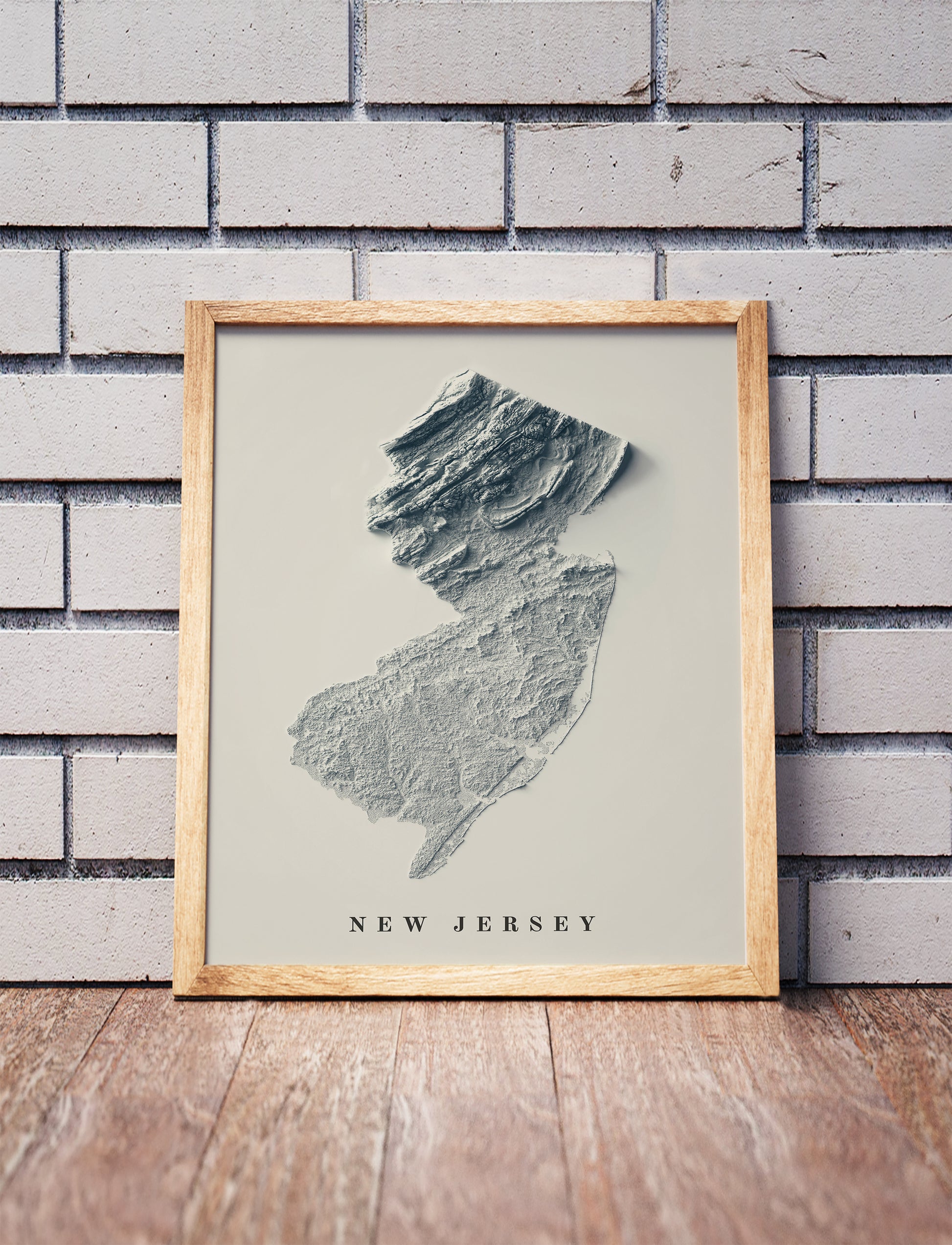 New Jersey shaded relief map in a wooden frame. Realistic terrain art print for home decor, displayed against a brick wall