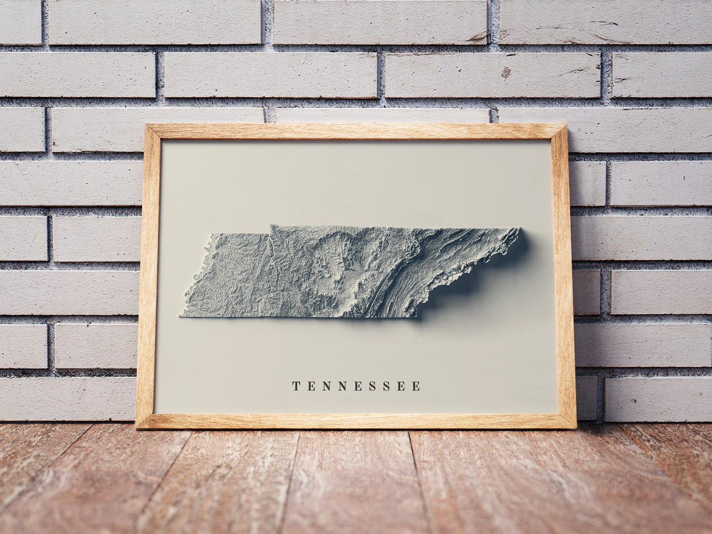 Tennessee shaded relief map in a wooden frame. Realistic terrain art print for home decor, displayed against a brick wall