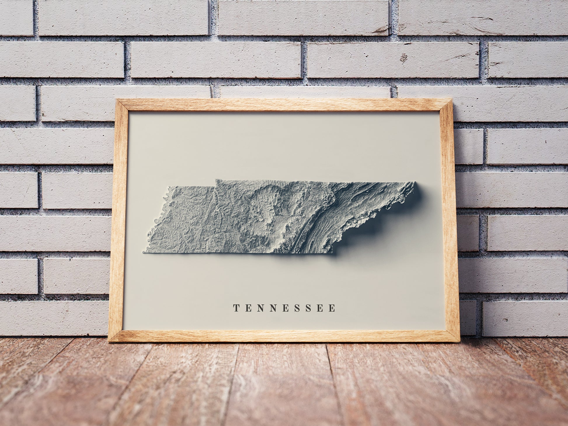 Tennessee shaded relief map in a wooden frame. Realistic terrain art print for home decor, displayed against a brick wall