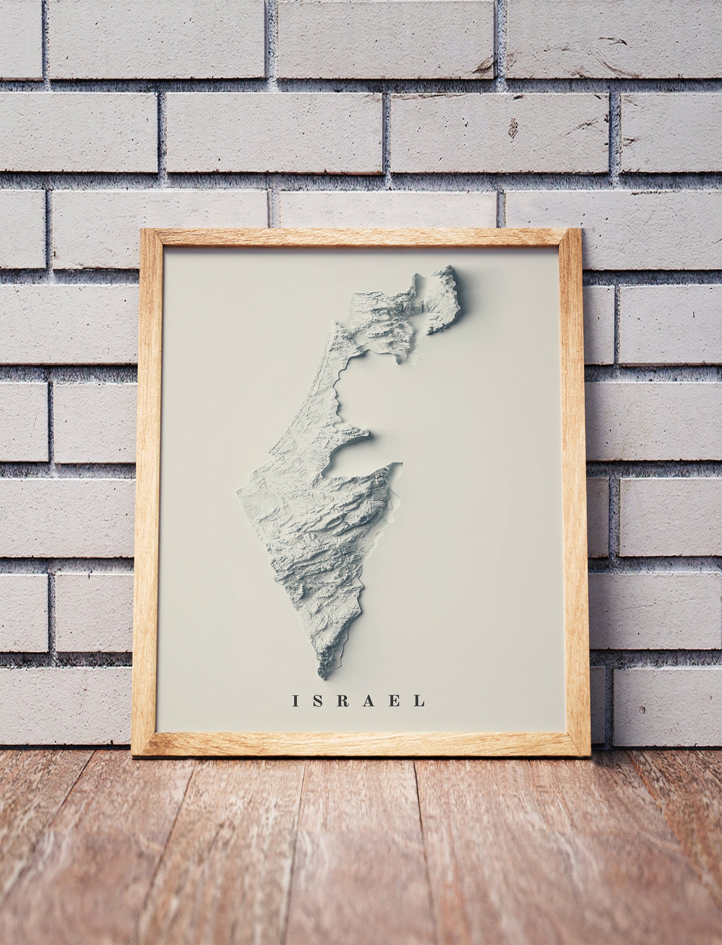 Israel shaded relief map in a wooden frame. Realistic terrain art print for home decor, displayed against a brick wall
