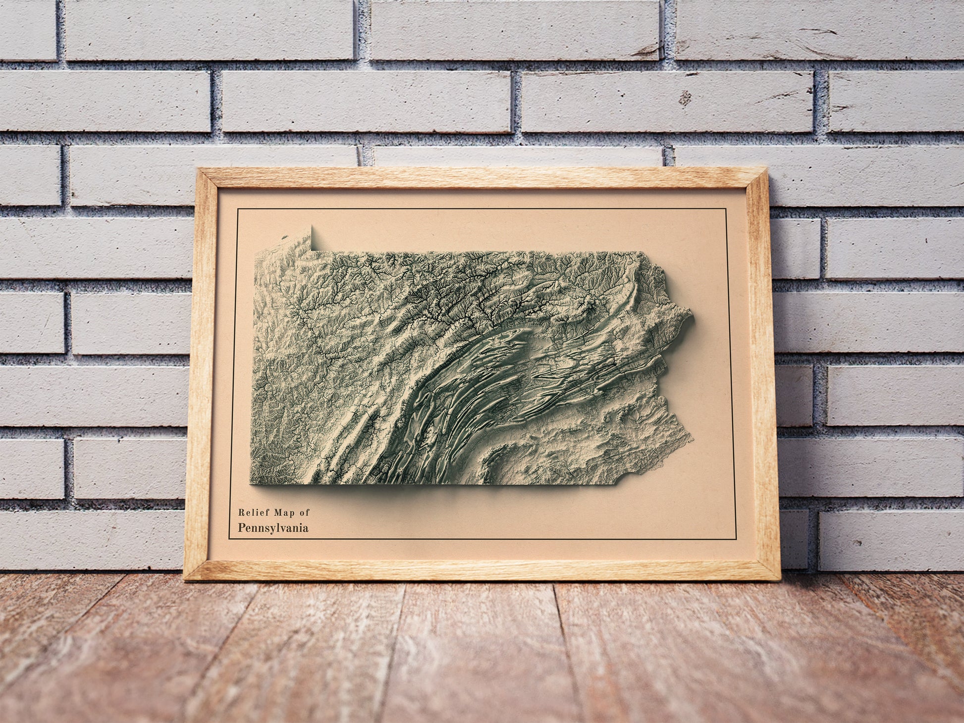 Vintage Pennsylvania shaded relief map in a wooden frame. Realistic terrain art print for home decor, displayed against a brick wall