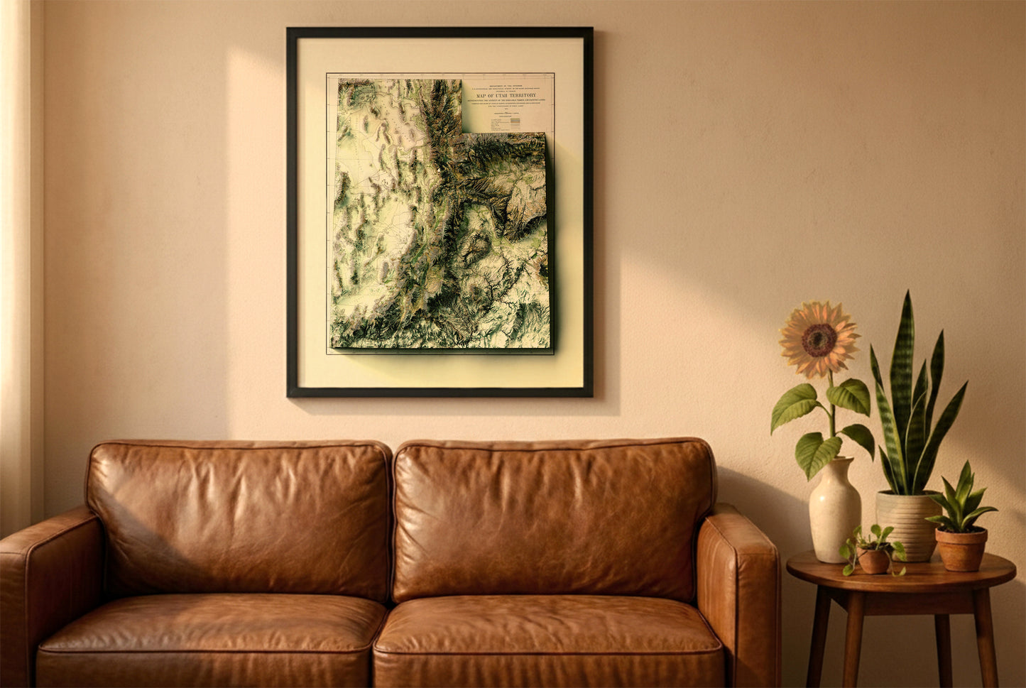 Utah vintage relief map in a black frame above a brown leather sofa. Boho living room with warm sunlight, sunflower, and indoor plants on a wooden side table