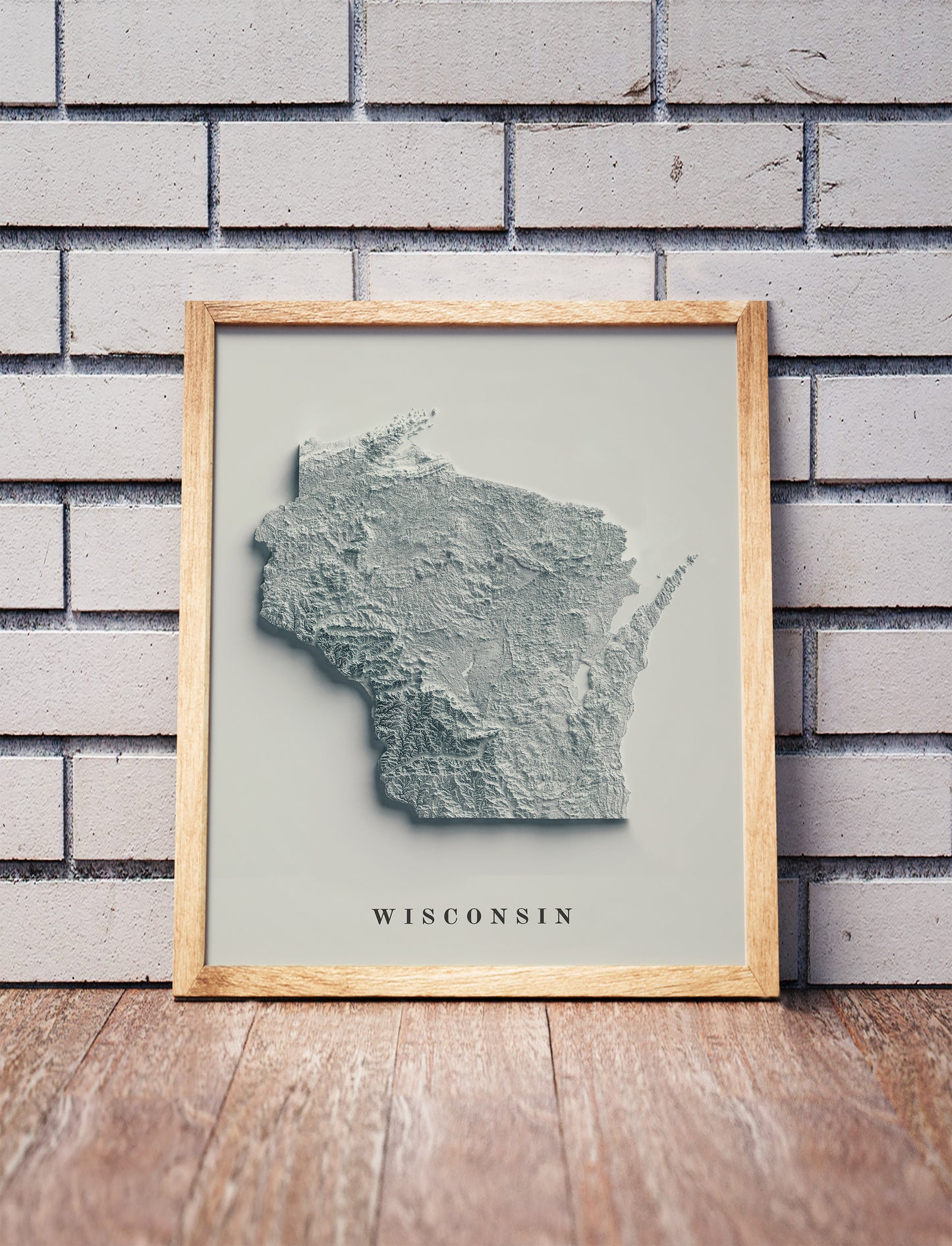 Wisconsin shaded relief map in a wooden frame. Realistic terrain art print for home decor, displayed against a brick wall