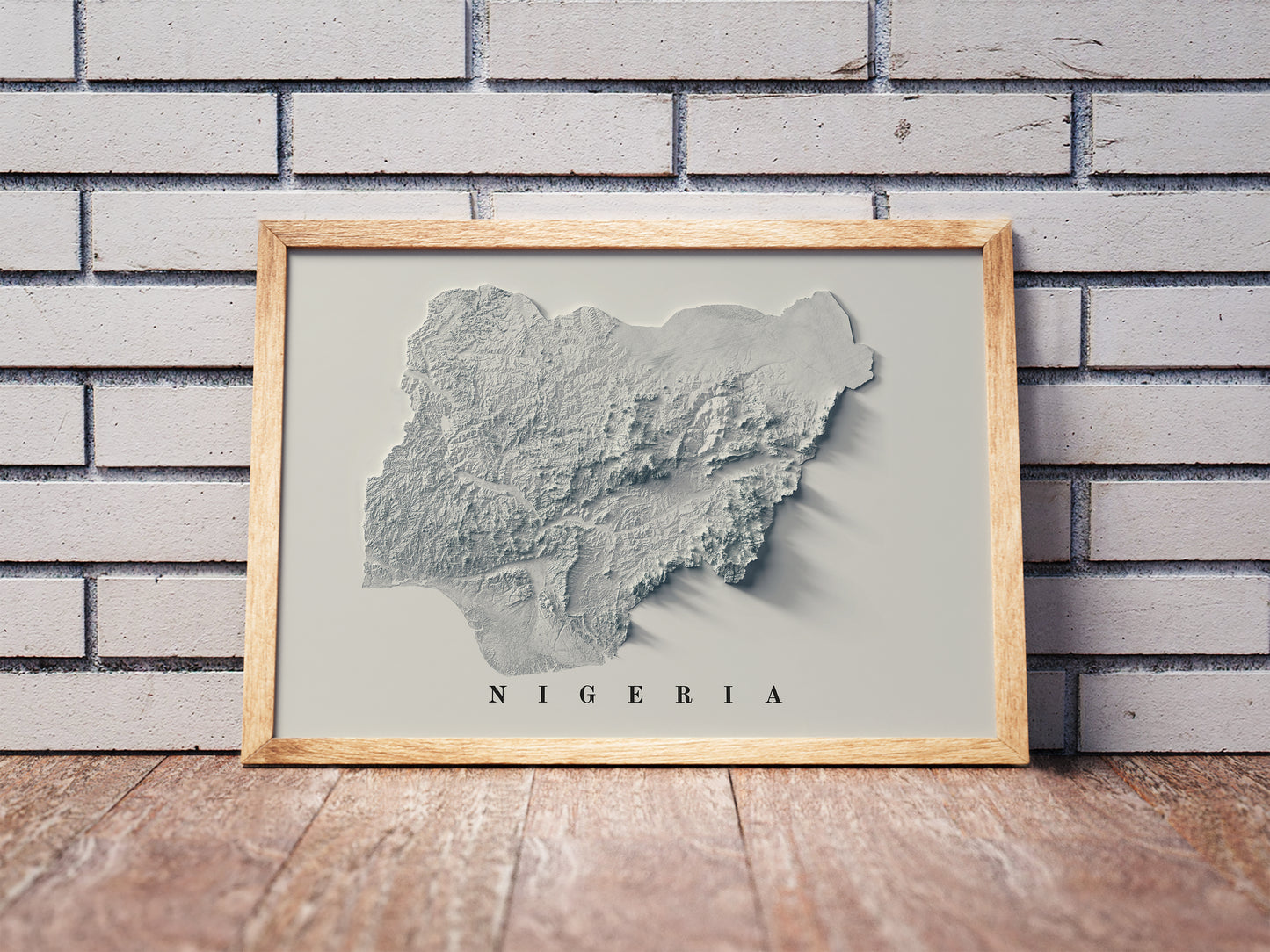 Nigeria shaded relief map in a wooden frame. Realistic terrain art print for home decor, displayed against a brick wall