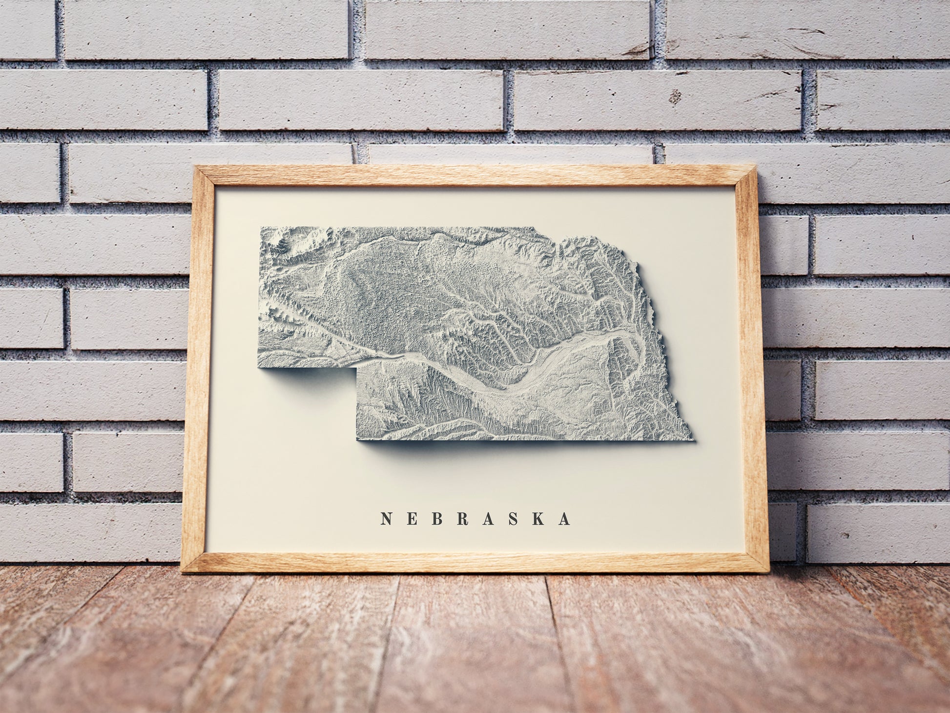 Nebraska shaded relief map in a wooden frame. Realistic terrain art print for home decor, displayed against a brick wall