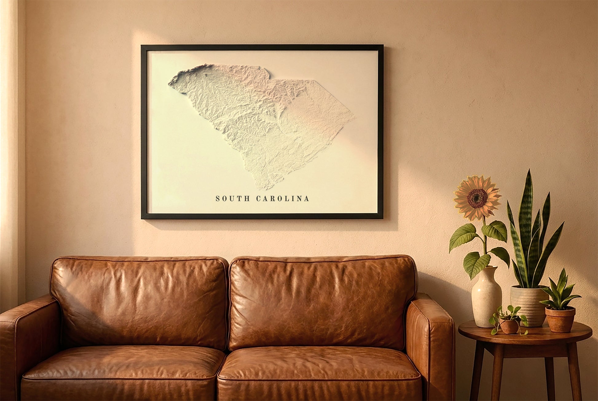 South Carolina relief map in a black frame above a brown leather sofa. Boho living room with warm sunlight, sunflower, and indoor plants on a wooden side table