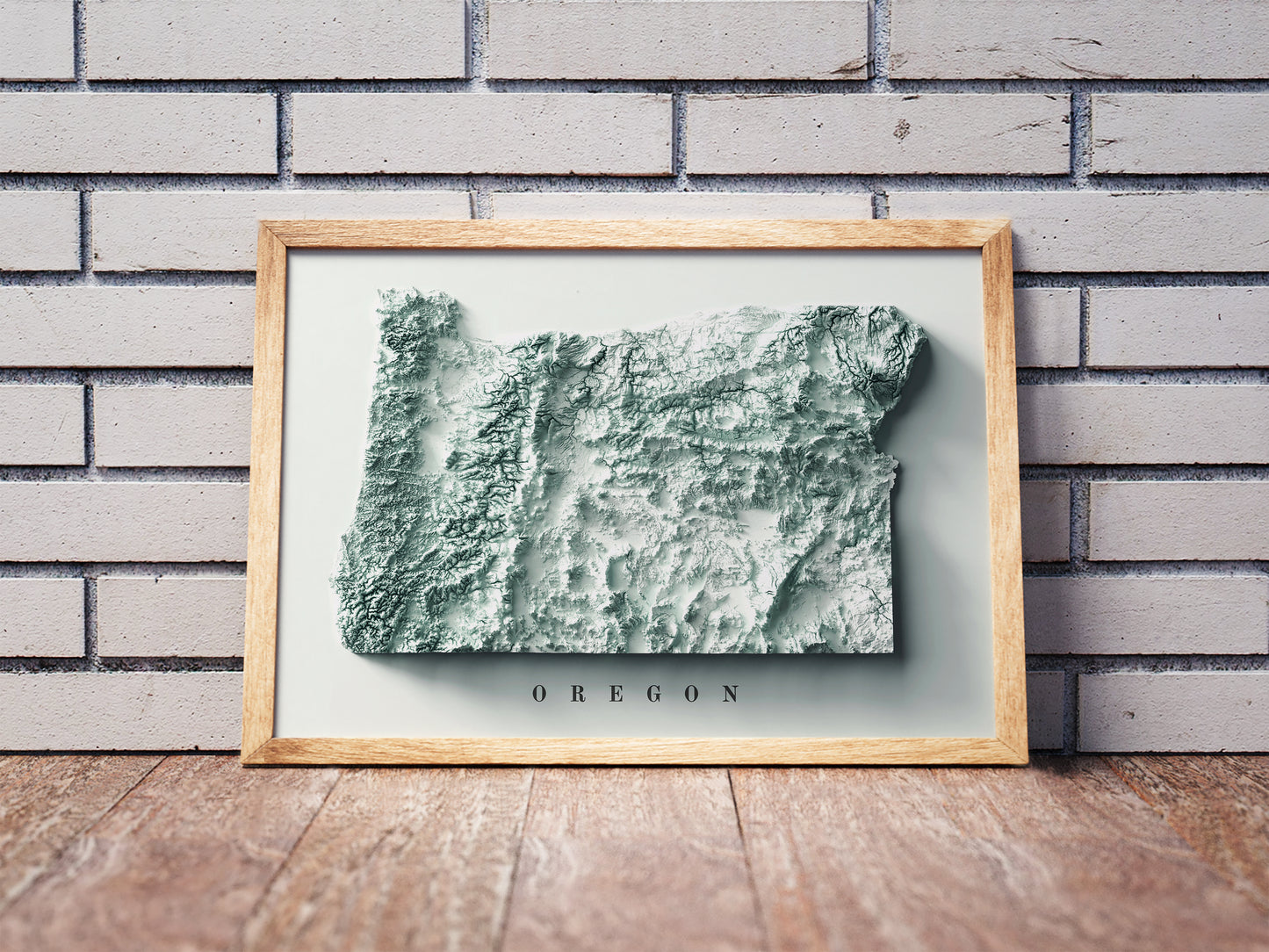 Oregon shaded relief map in a wooden frame. Realistic terrain art print for home decor, displayed against a brick wall