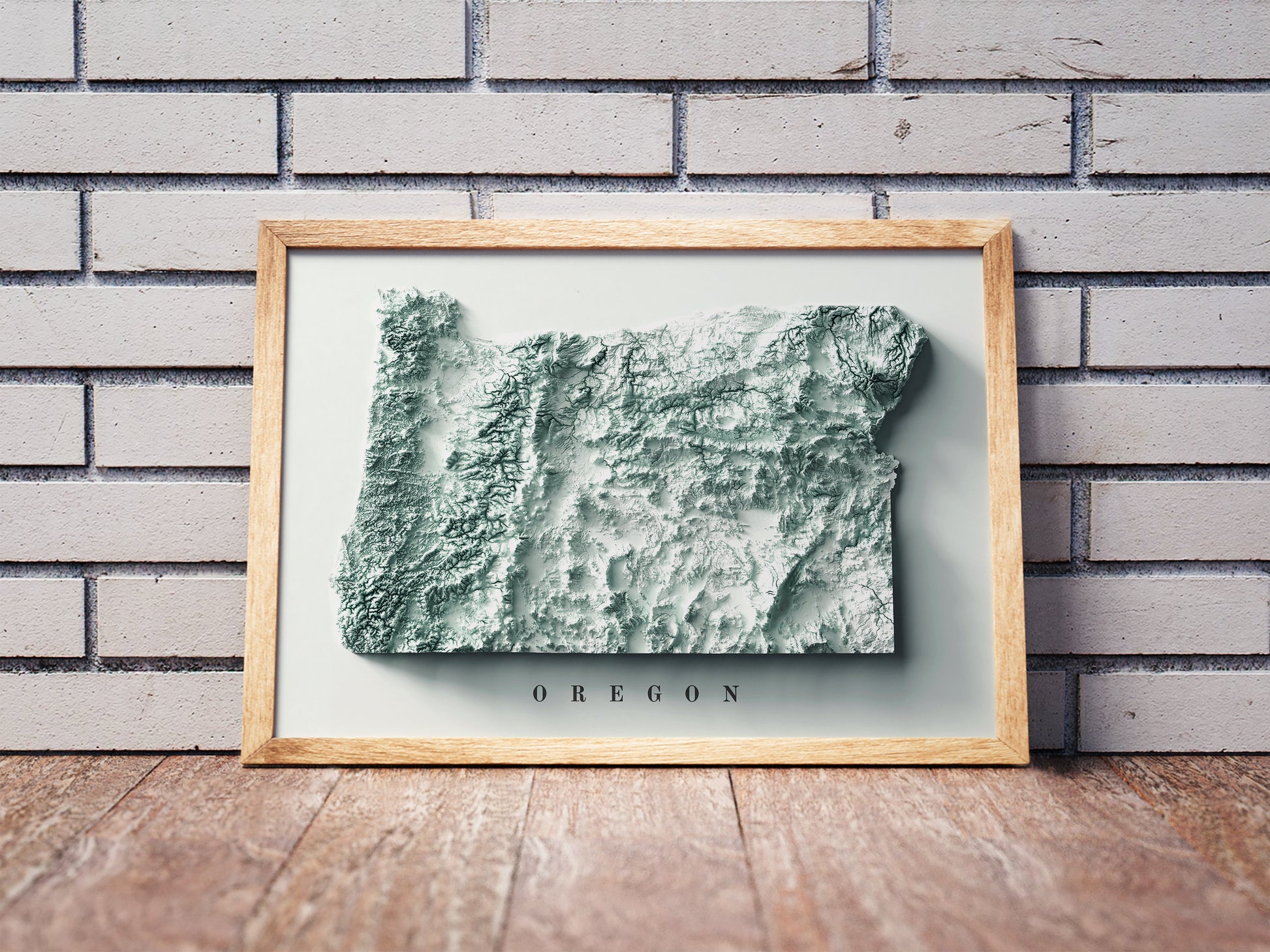 Oregon shaded relief map in a wooden frame. Realistic terrain art print for home decor, displayed against a brick wall
