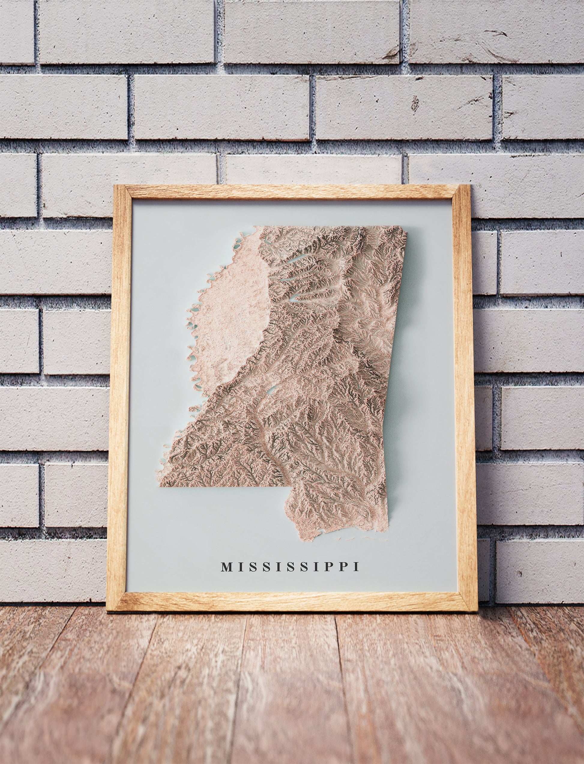 Mississippi shaded relief map in a wooden frame. Realistic terrain art print for home decor, displayed against a brick wall