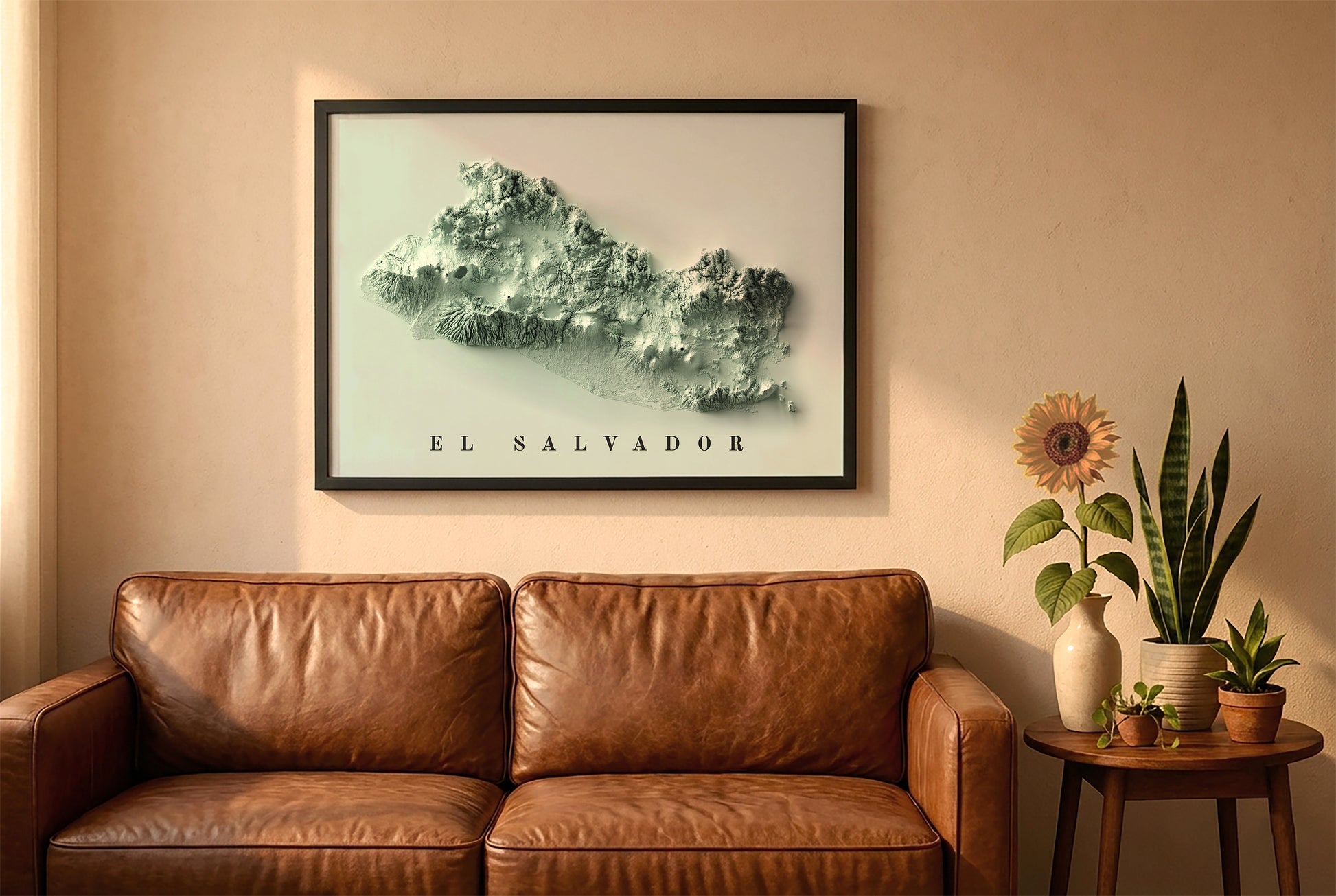El Salvador relief map in a black frame above a brown leather sofa. Boho living room with warm sunlight, sunflower, and indoor plants on a wooden side table