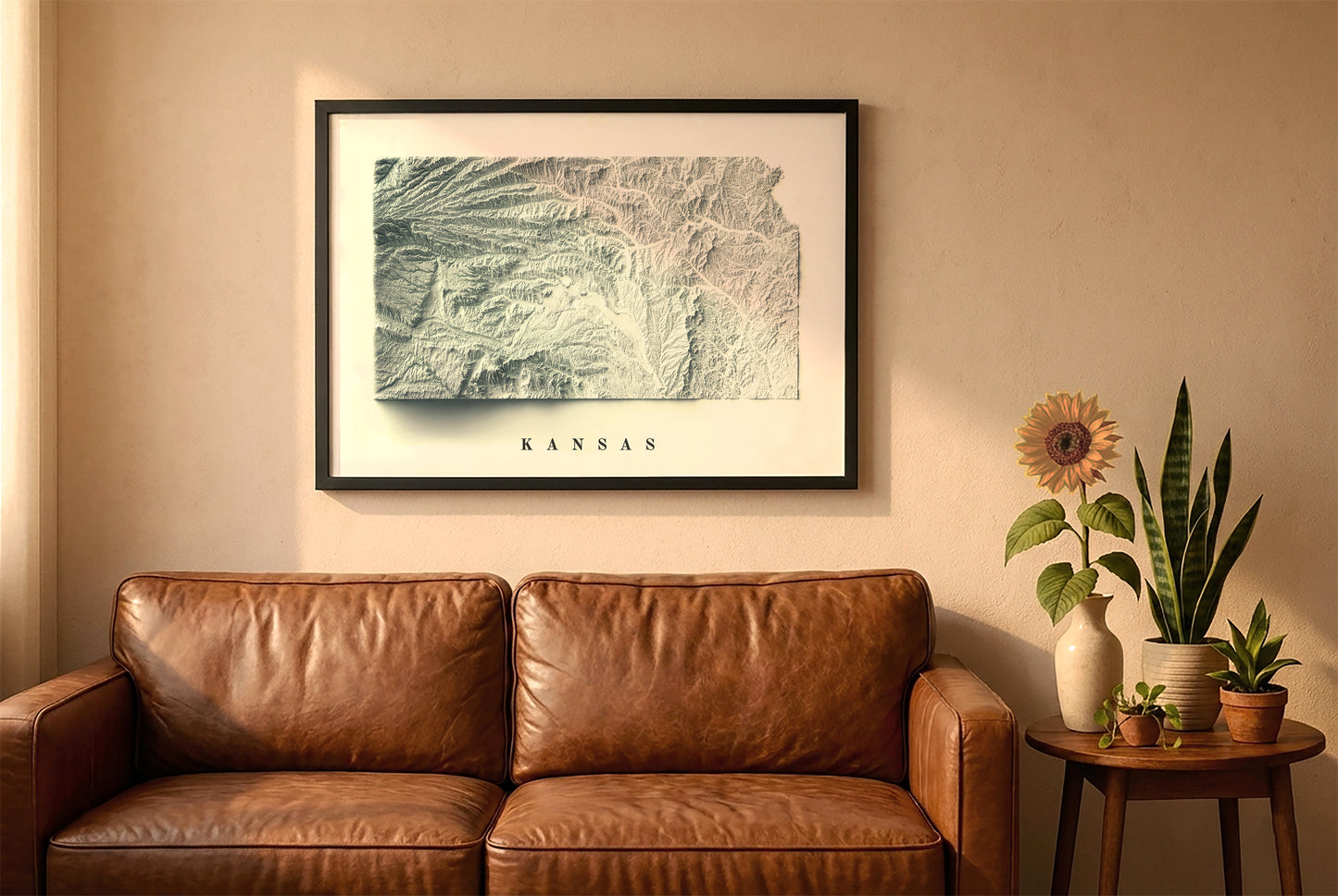 Kansas relief map in a black frame above a brown leather sofa. Boho living room with warm sunlight, sunflower, and indoor plants on a wooden side table